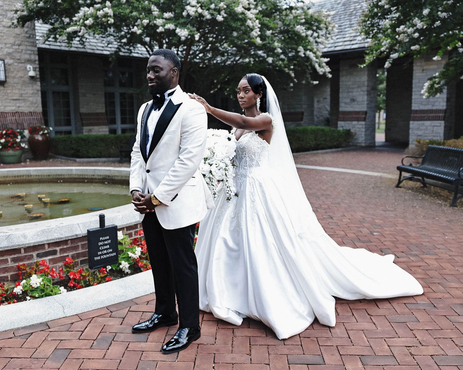 Bride in a white wedding gown tapping  groom's shoulder for first look in a brick courtyard.