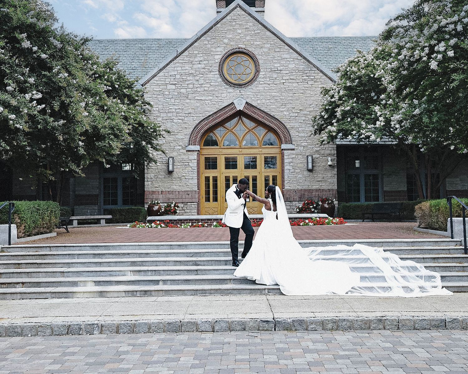 Bride and groom posing on the steps outside a stone church, with the bride's wedding dress spread behind her.