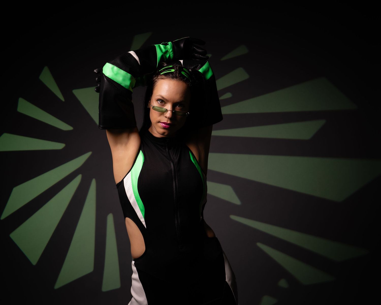 Woman in black and green athletic outfit poses against geometric green patterned dark background.