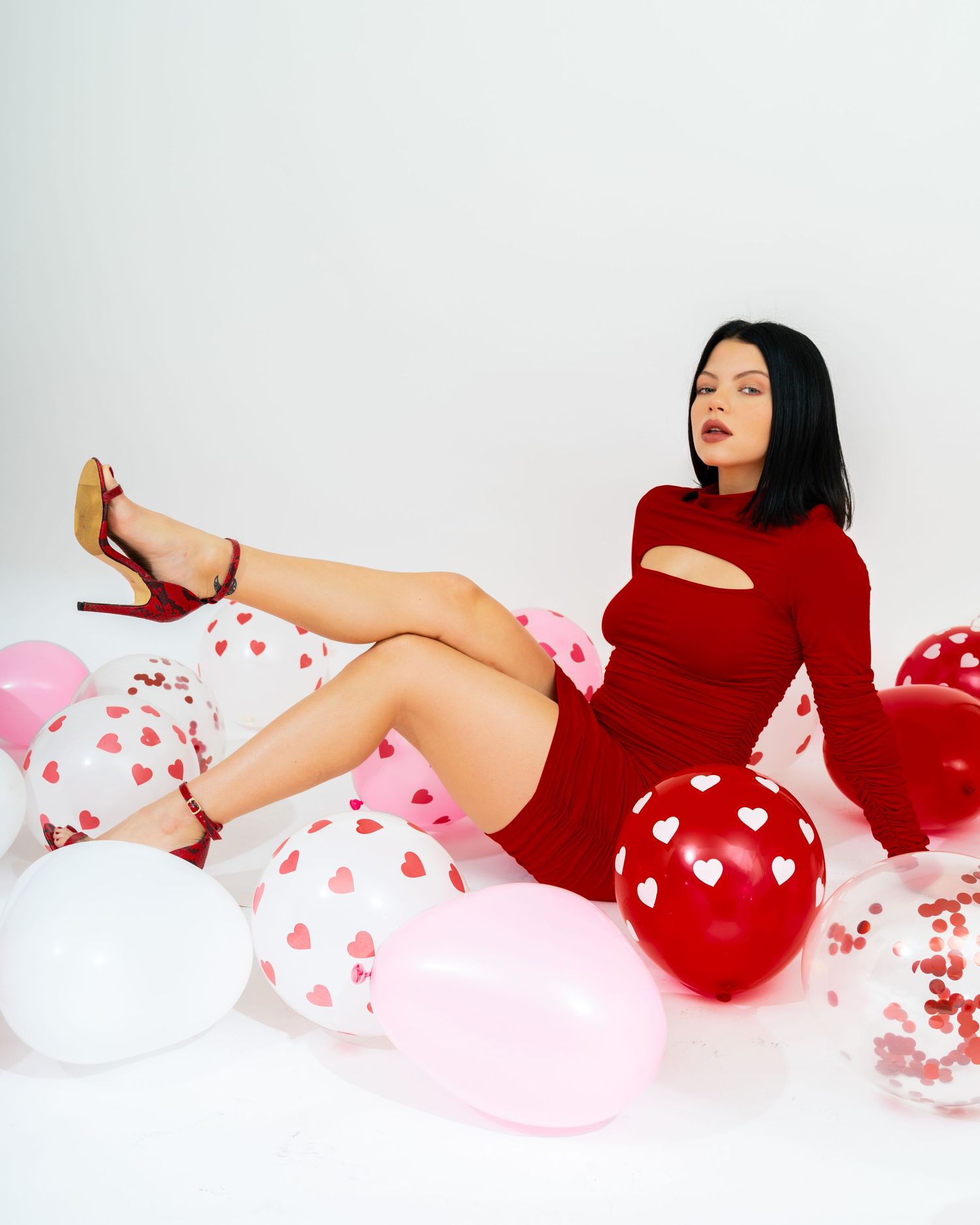 Brunette woman in red cutout dress posing with Valentine's Day balloons.
