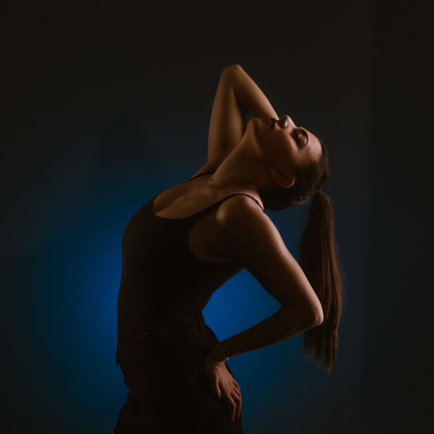 Woman dancer posing dramatically against dark background with blue accent lighting.