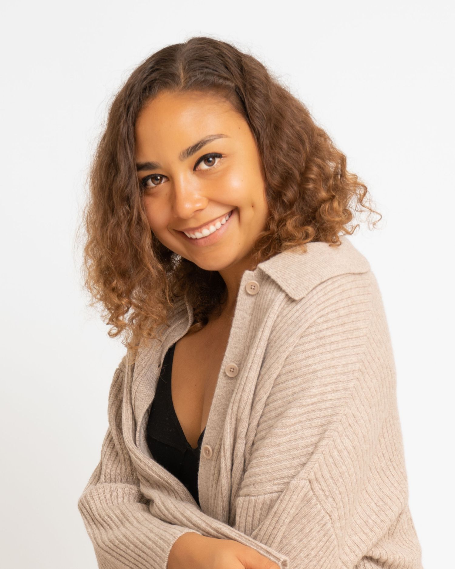 Smiling woman with curly hair in beige cardigan on white background.
