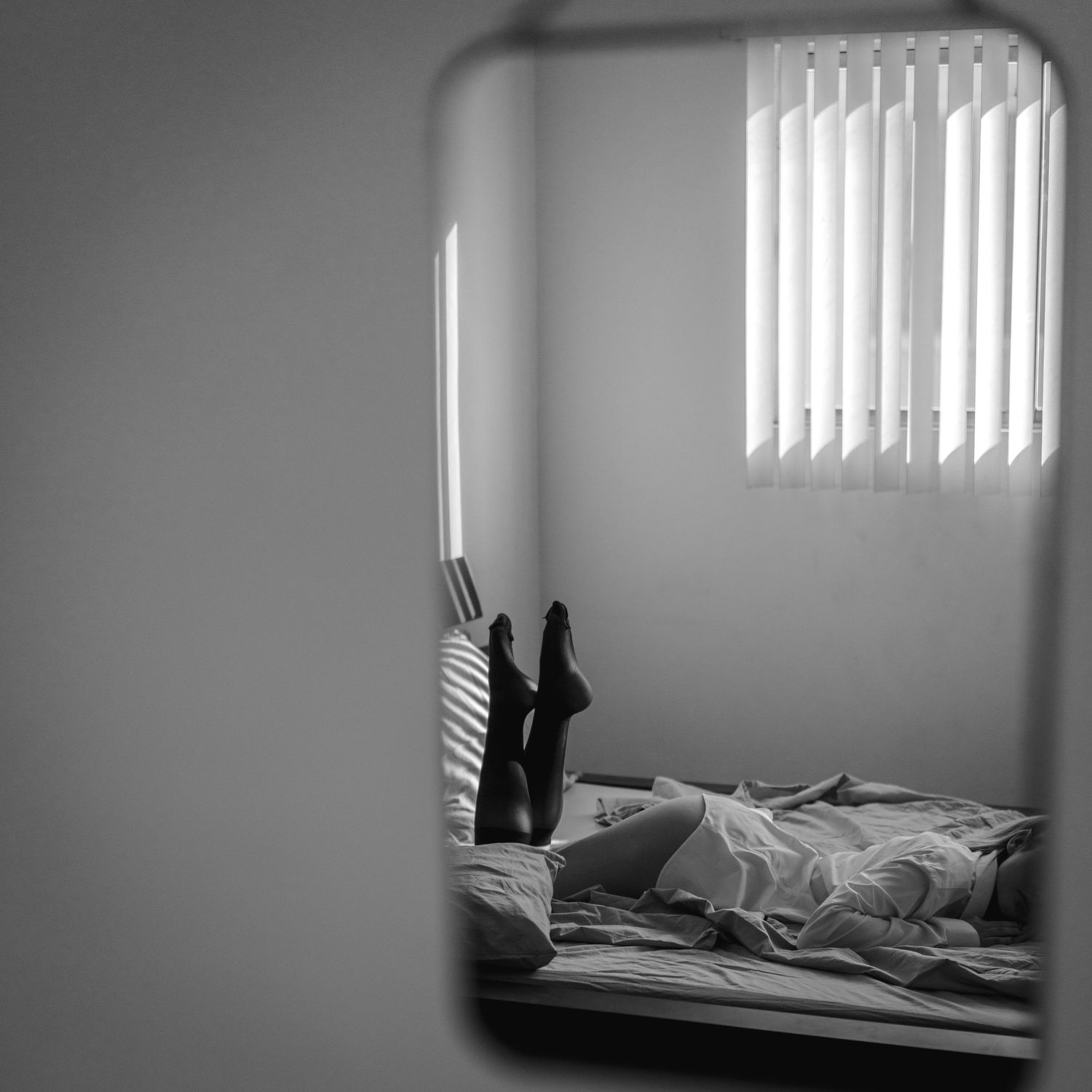 Black and white mirror reflection of person lying on bed near window.