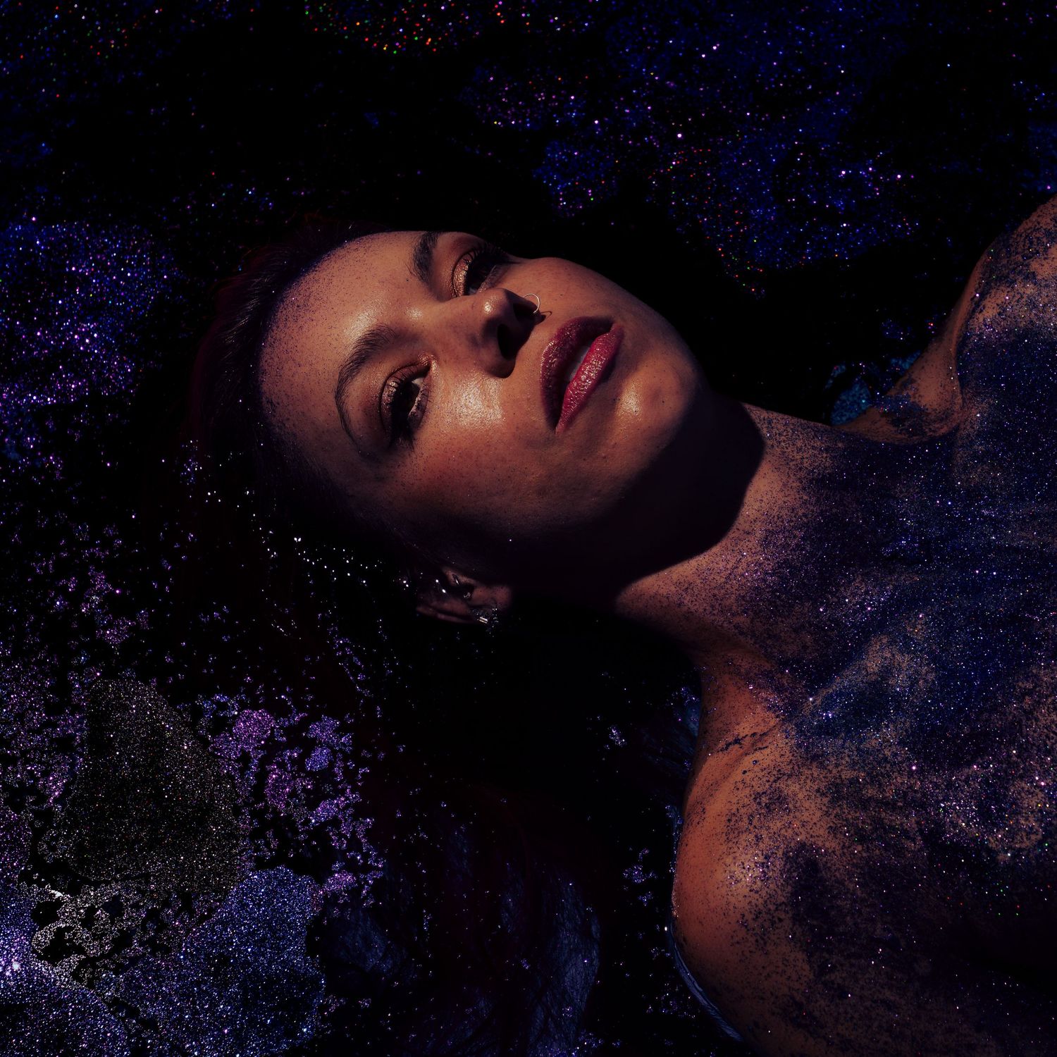 Woman lying in dark blue glittery water with dramatic moody lighting.
