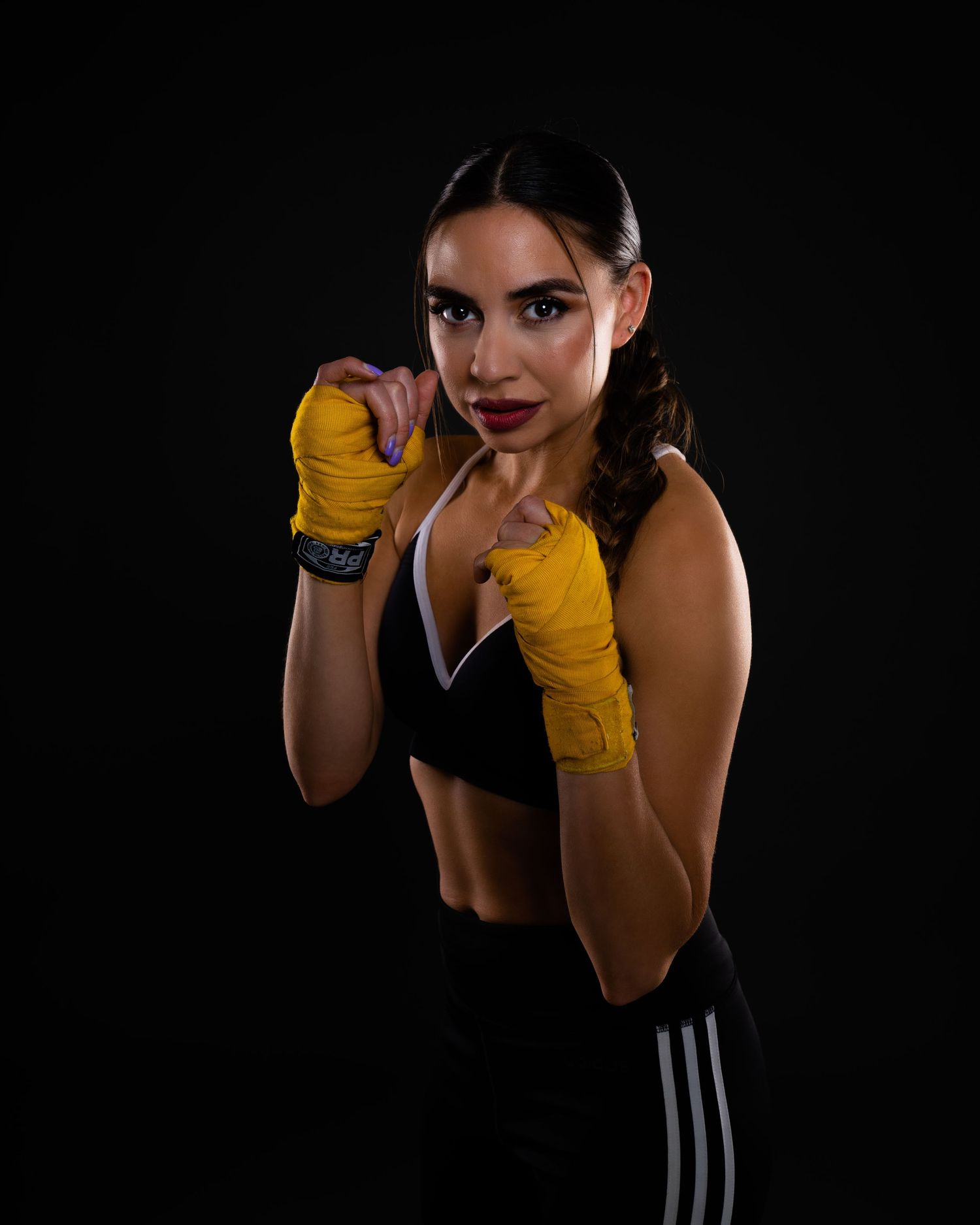 Athletic woman in boxing hand wraps poses in fighting stance against dark background.