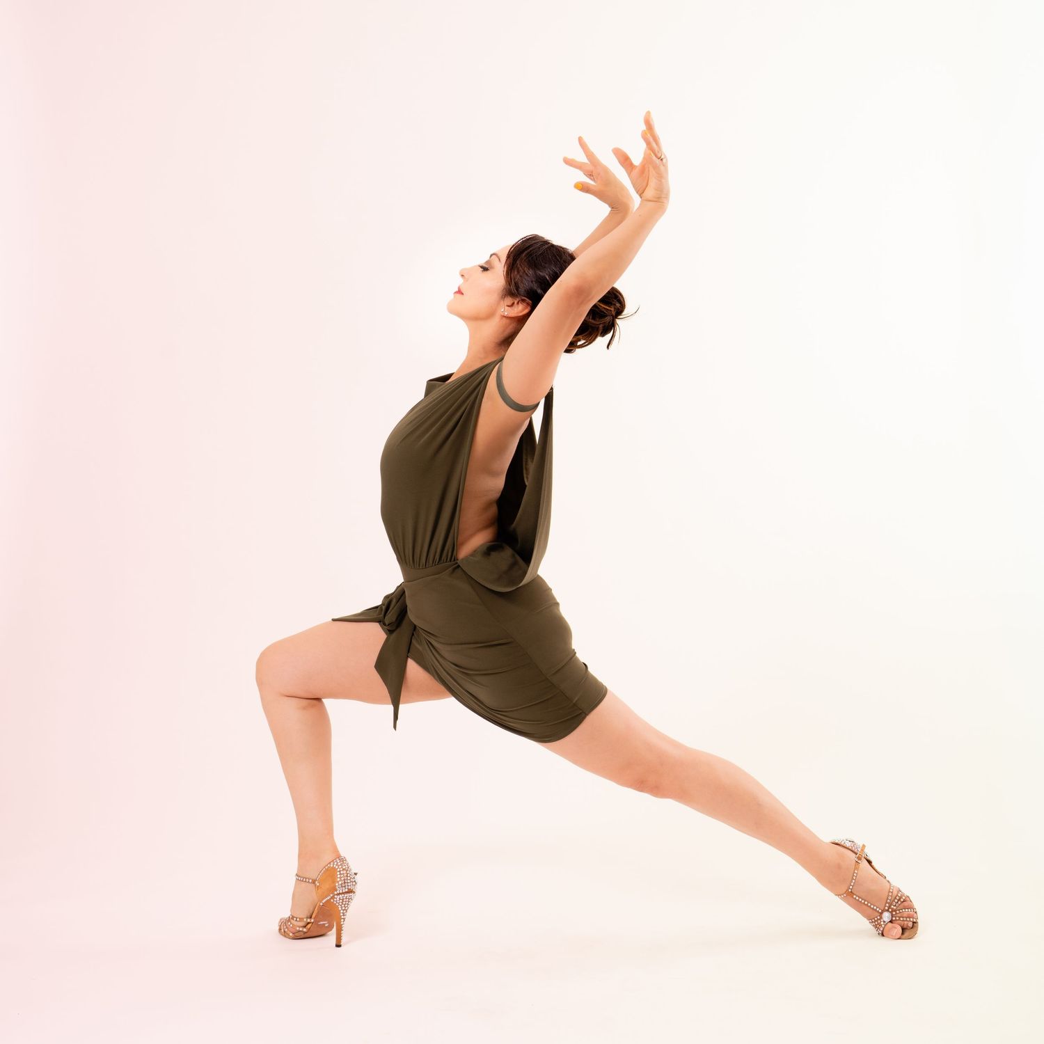 Woman in olive green dress performing dynamic dance lunge pose.