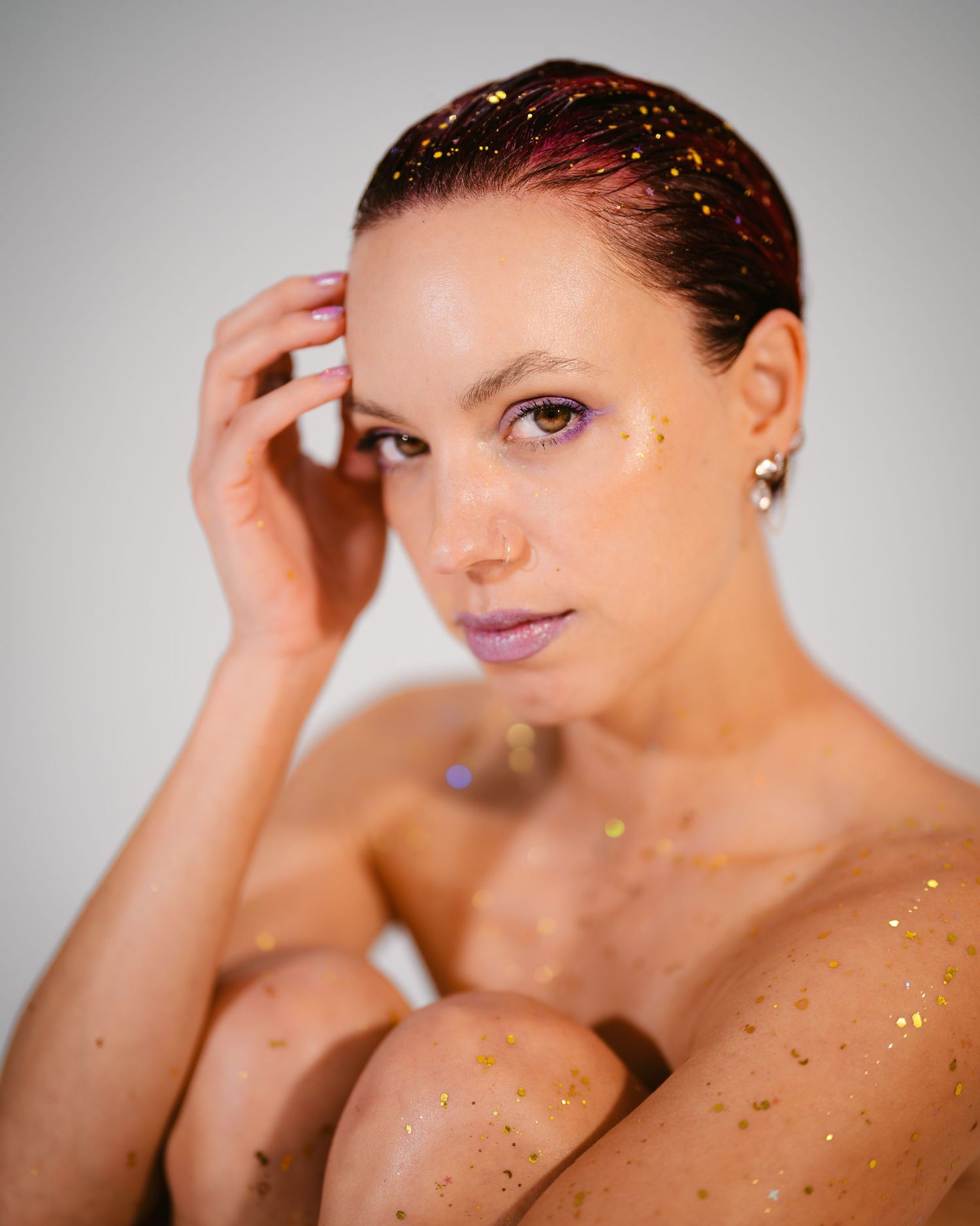 Woman with gold glitter on skin and hair posing against white background.