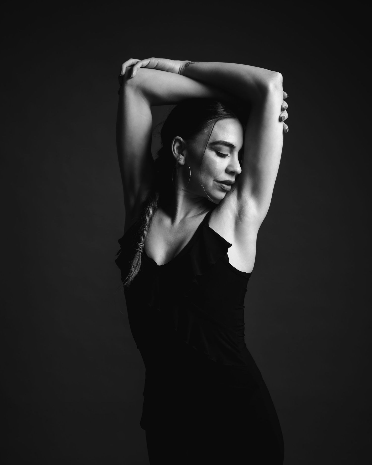 Black and white portrait of a woman in black stretching her arms overhead gracefully.