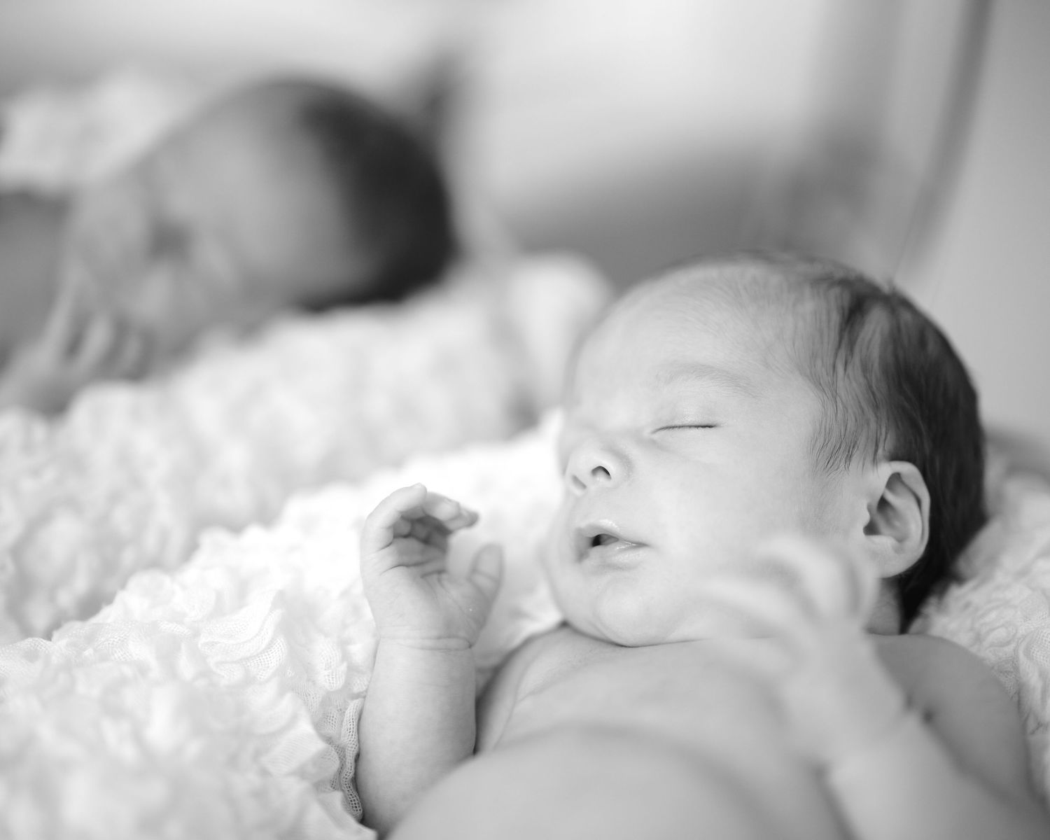 A serene black and white close-up of two sleeping newborn babies resting on a soft blanket.