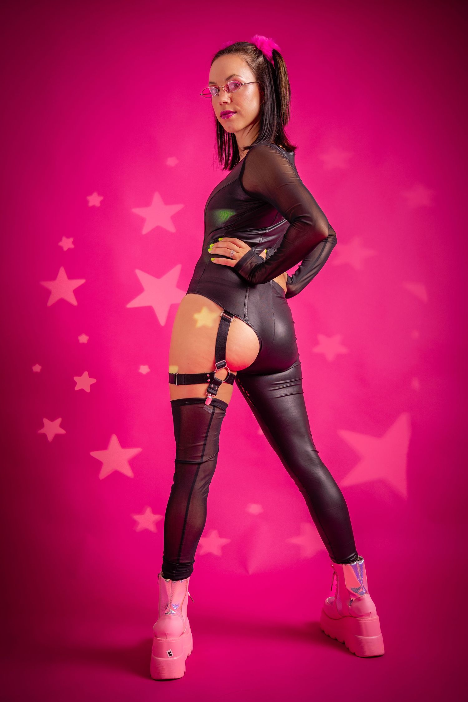 Woman in black latex outfit with garter belt and pink platform boots on pink star background.