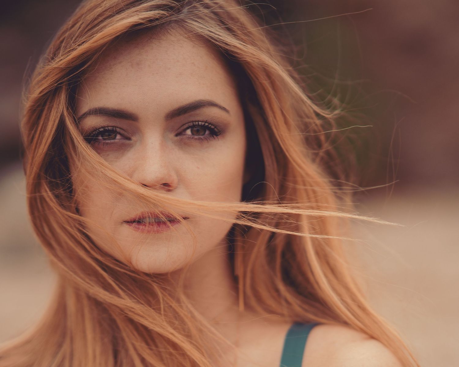 Close-up portrait of woman with auburn hair blowing across her face.
