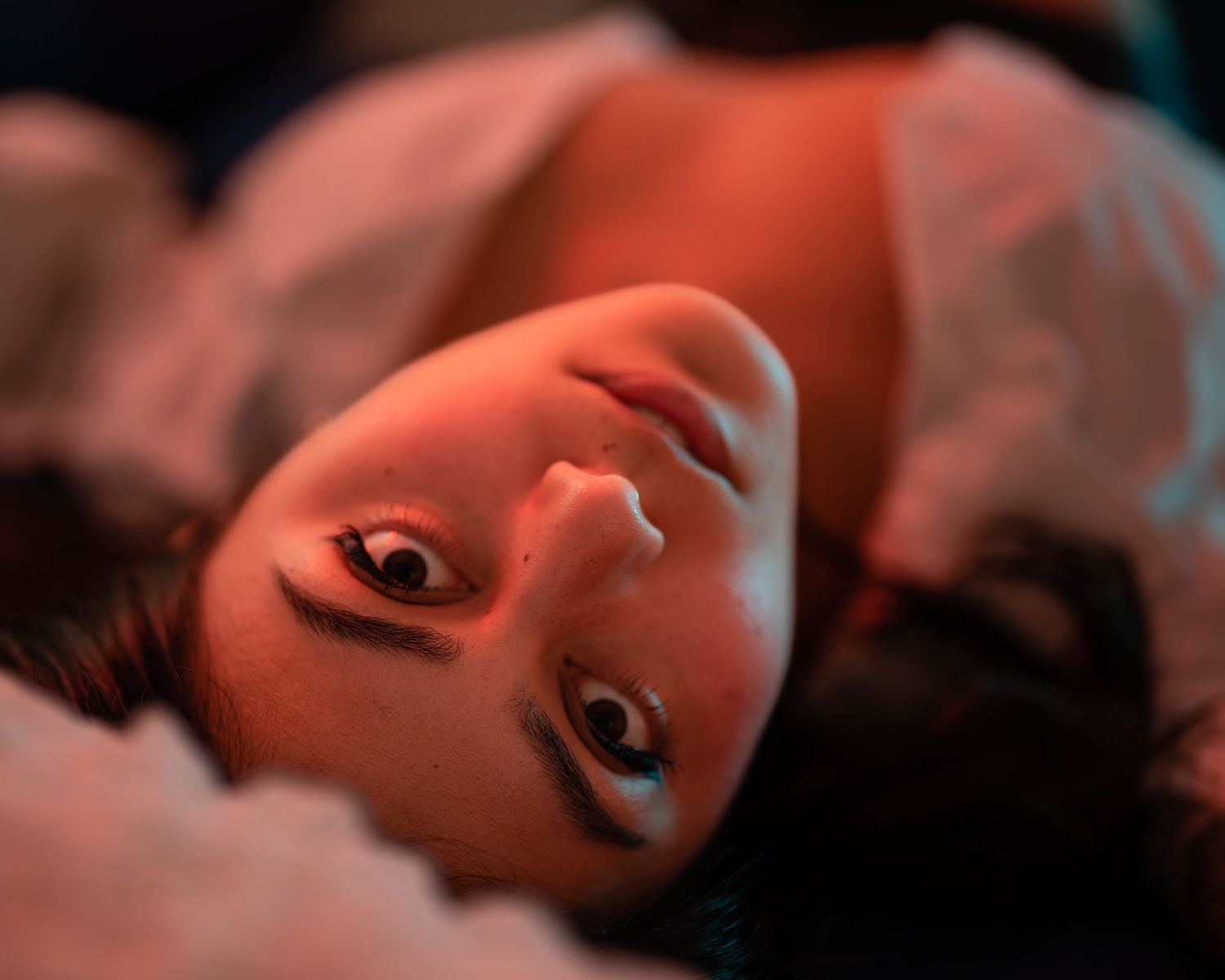 Young woman lying down with dramatic red lighting illuminating her face in a moody portrait.