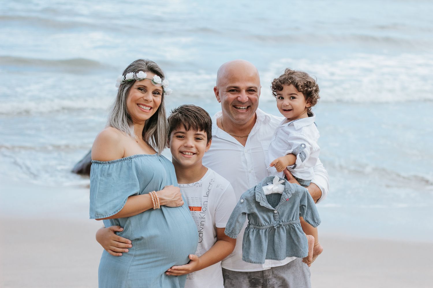 Família de mãe gestante, filho mais velho, filho pequeno e pai marido, praia ao fundo, em Ubatuba.
