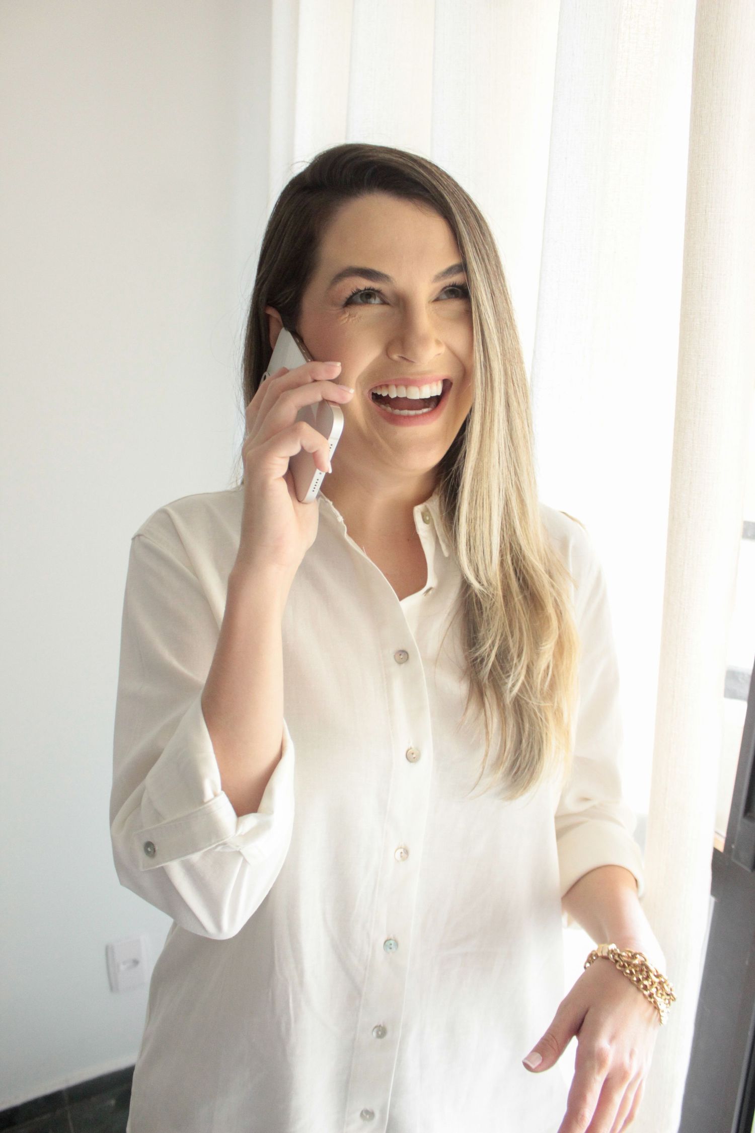 Retrato feminino de marca pessoal de uma mulher jovem, de cabelos loiros, sorrindo e falando ao celular, em Ubatuba.