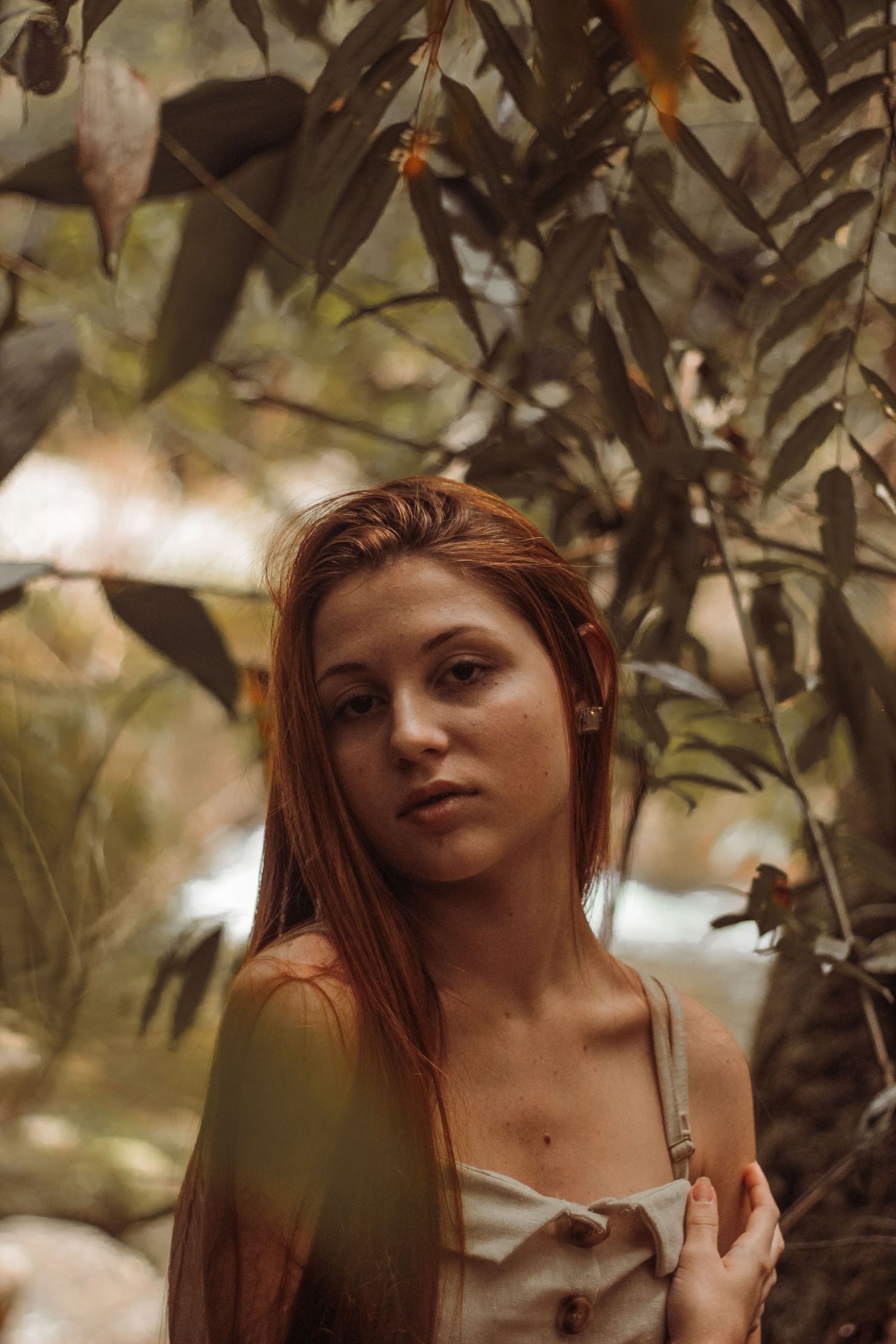 Retrato feminino em Ubatuba, mulher jovem, de cabelos ruivos, posando com face séria, com natureza ao fundo.