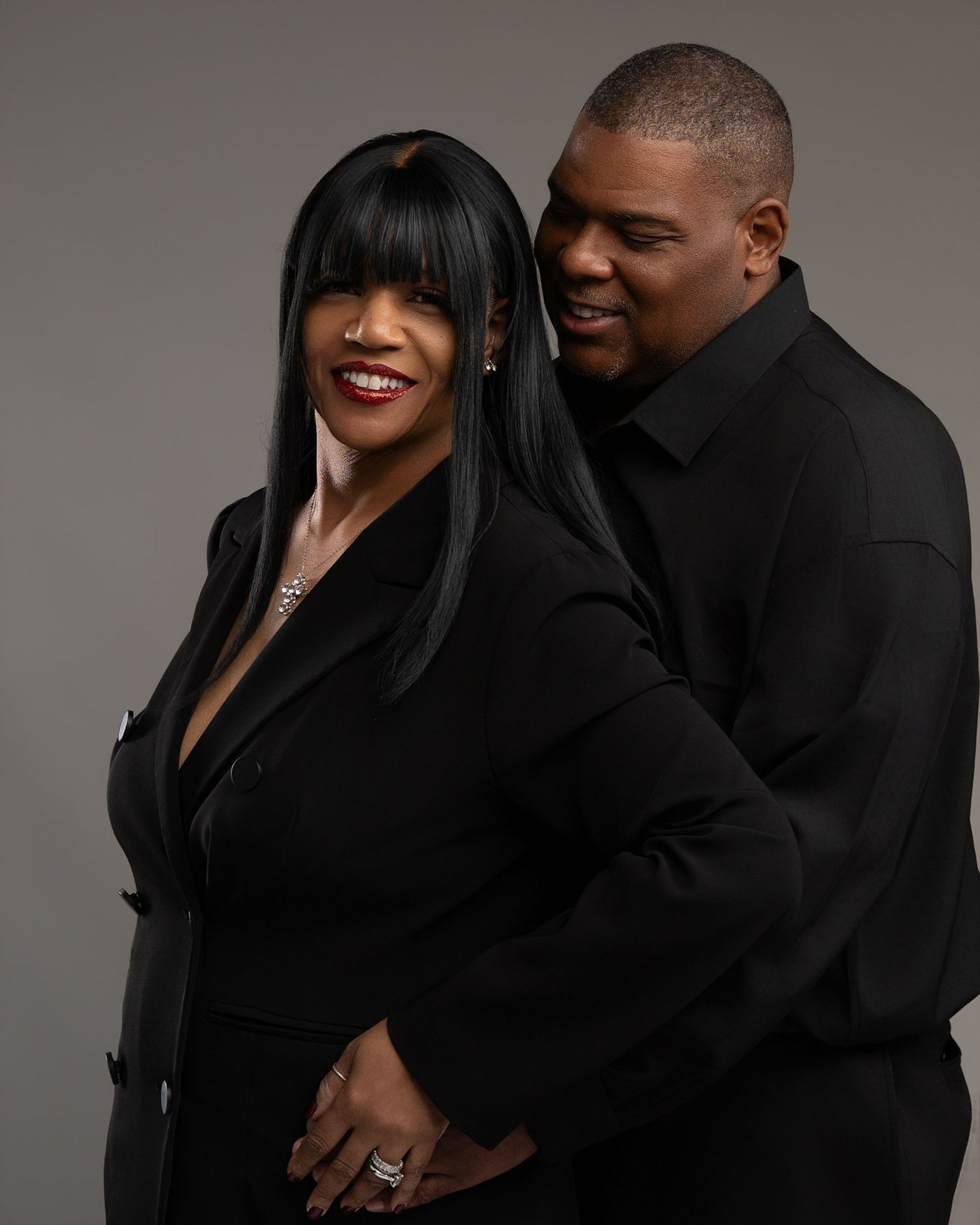 Elegant couple in matching black outfits posing together in a professional studio portrait photo.