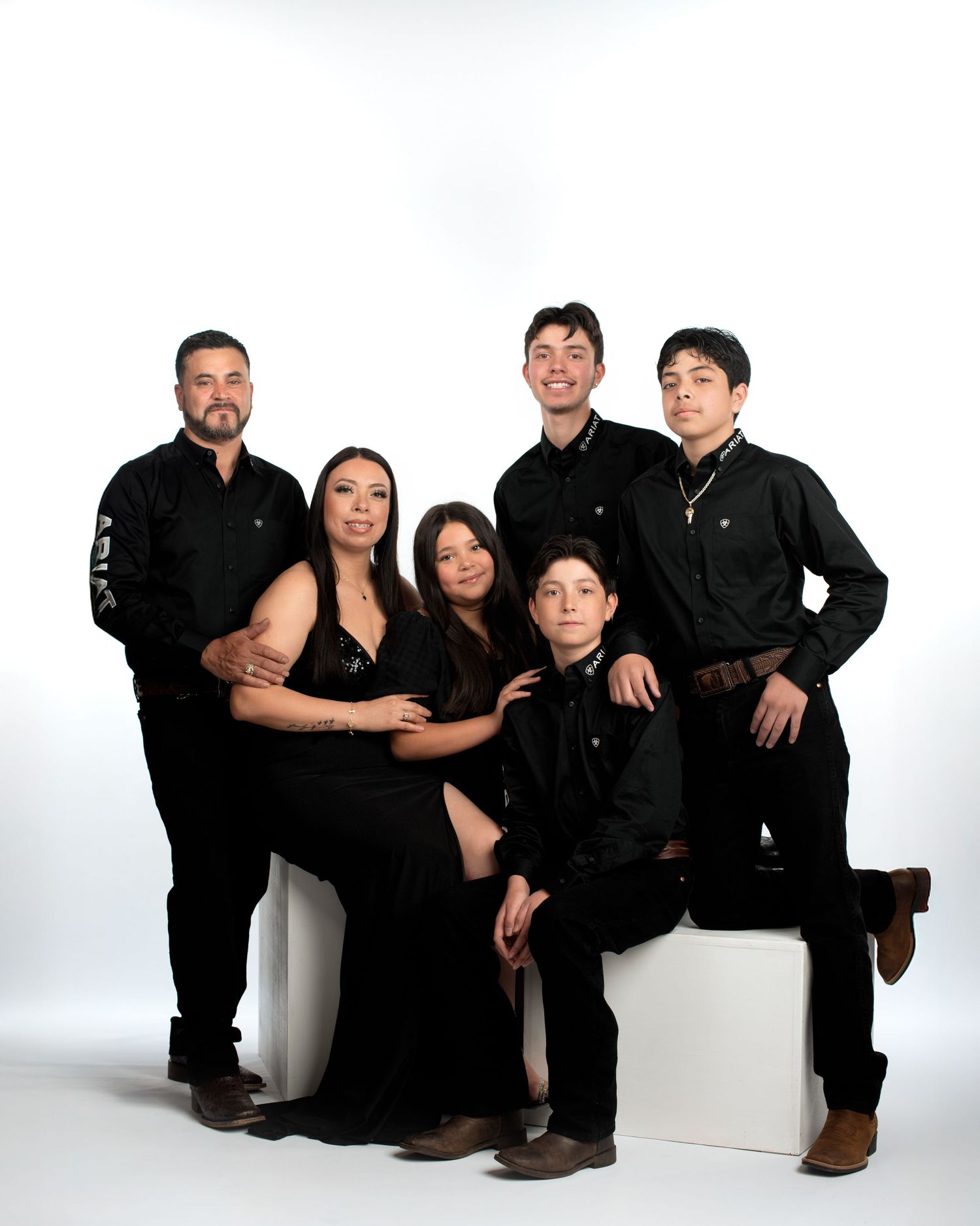 Family of six in matching black outfits posing together in a bright professional studio portrait.