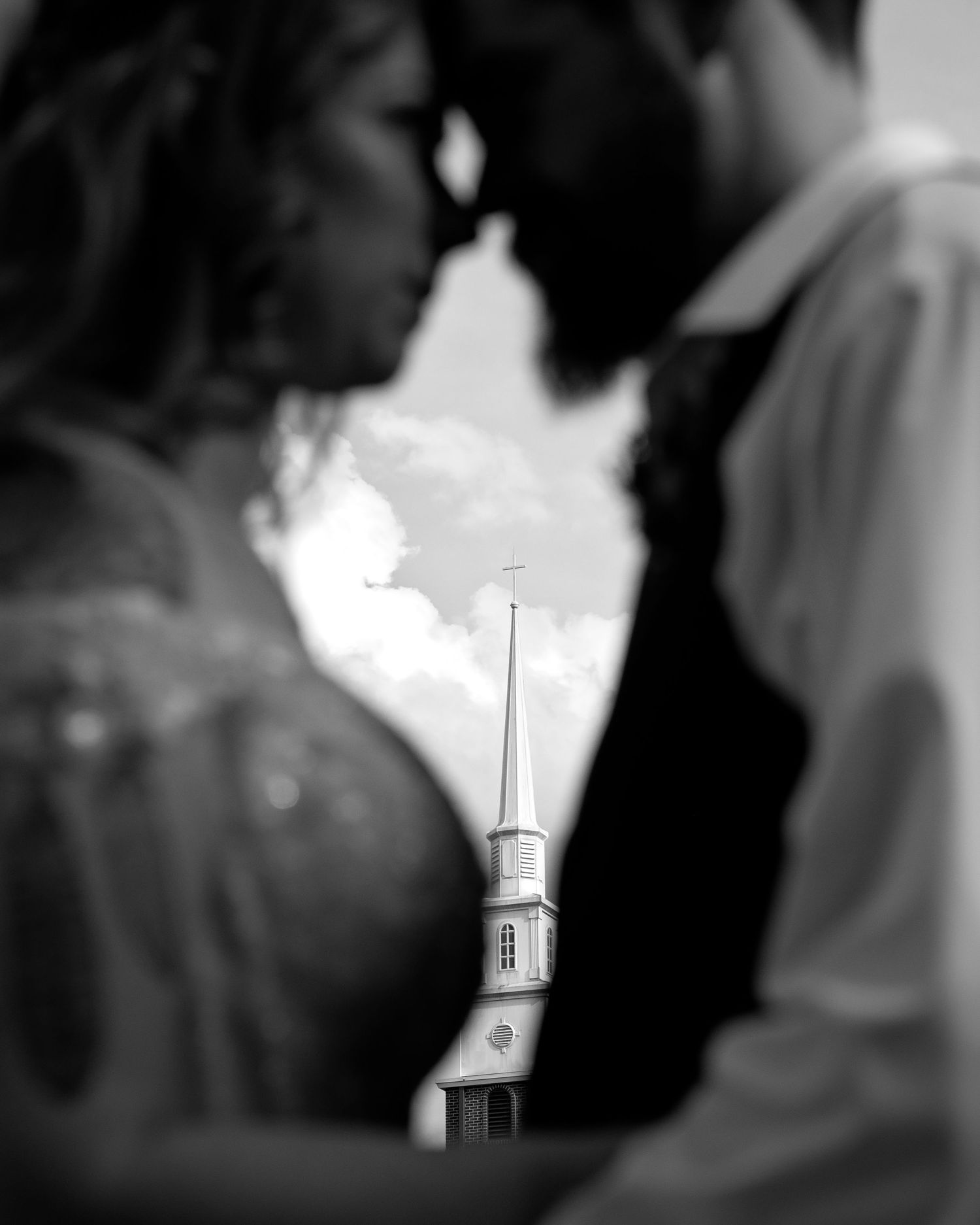 Black and white artistic wedding photo with church steeple framed between blurred couple.