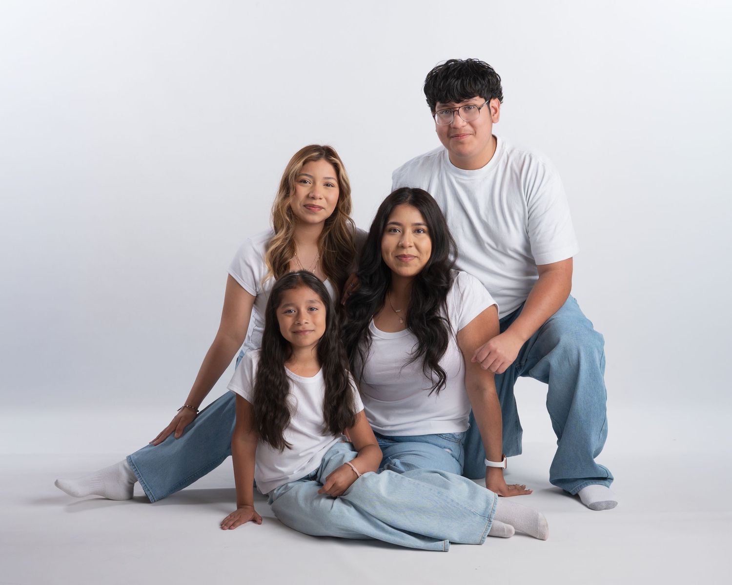 Four family members in white tops and jeans pose together in a casual studio portrait.