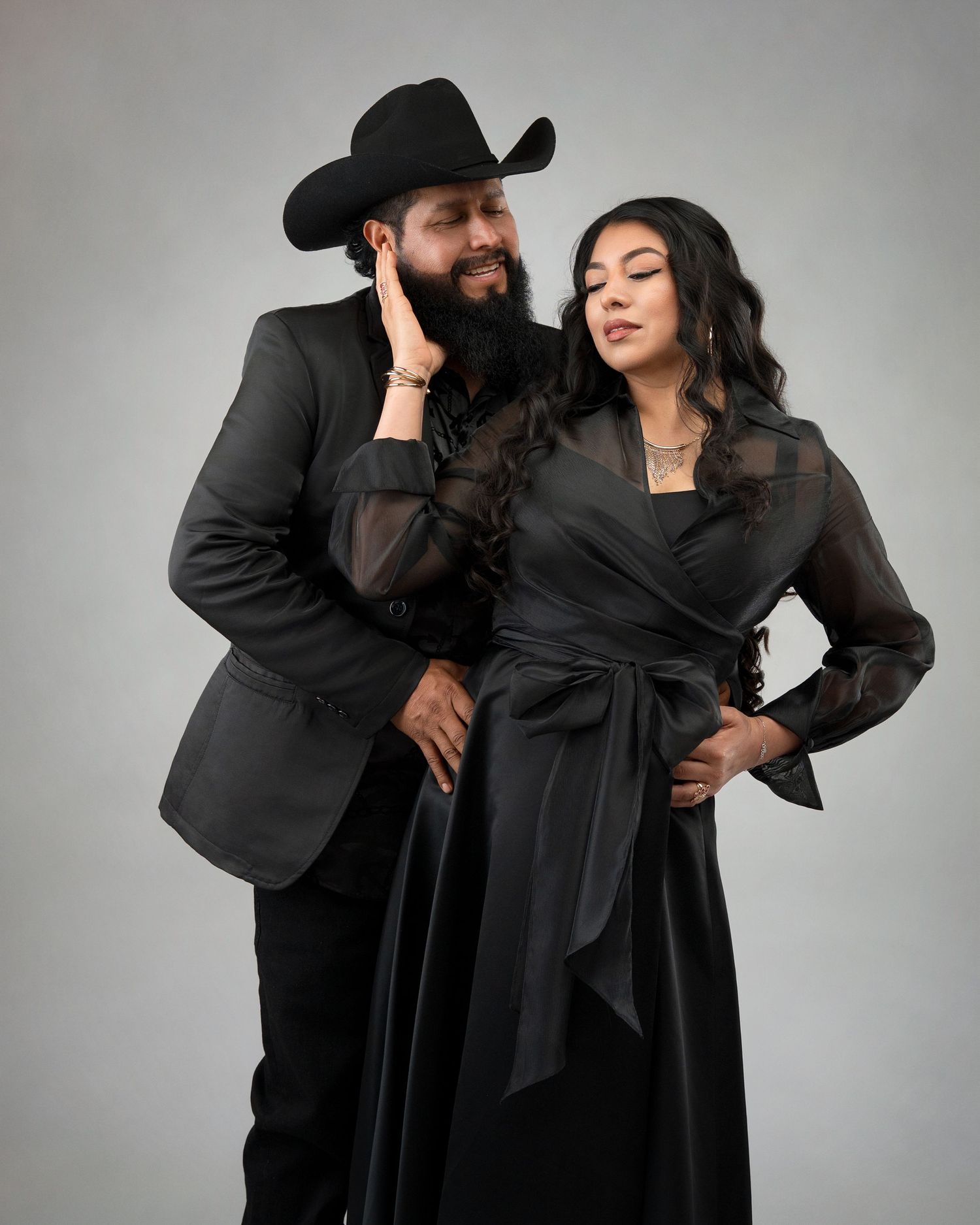 Stylish couple in all-black attire with man in cowboy hat posing in professional studio portrait.