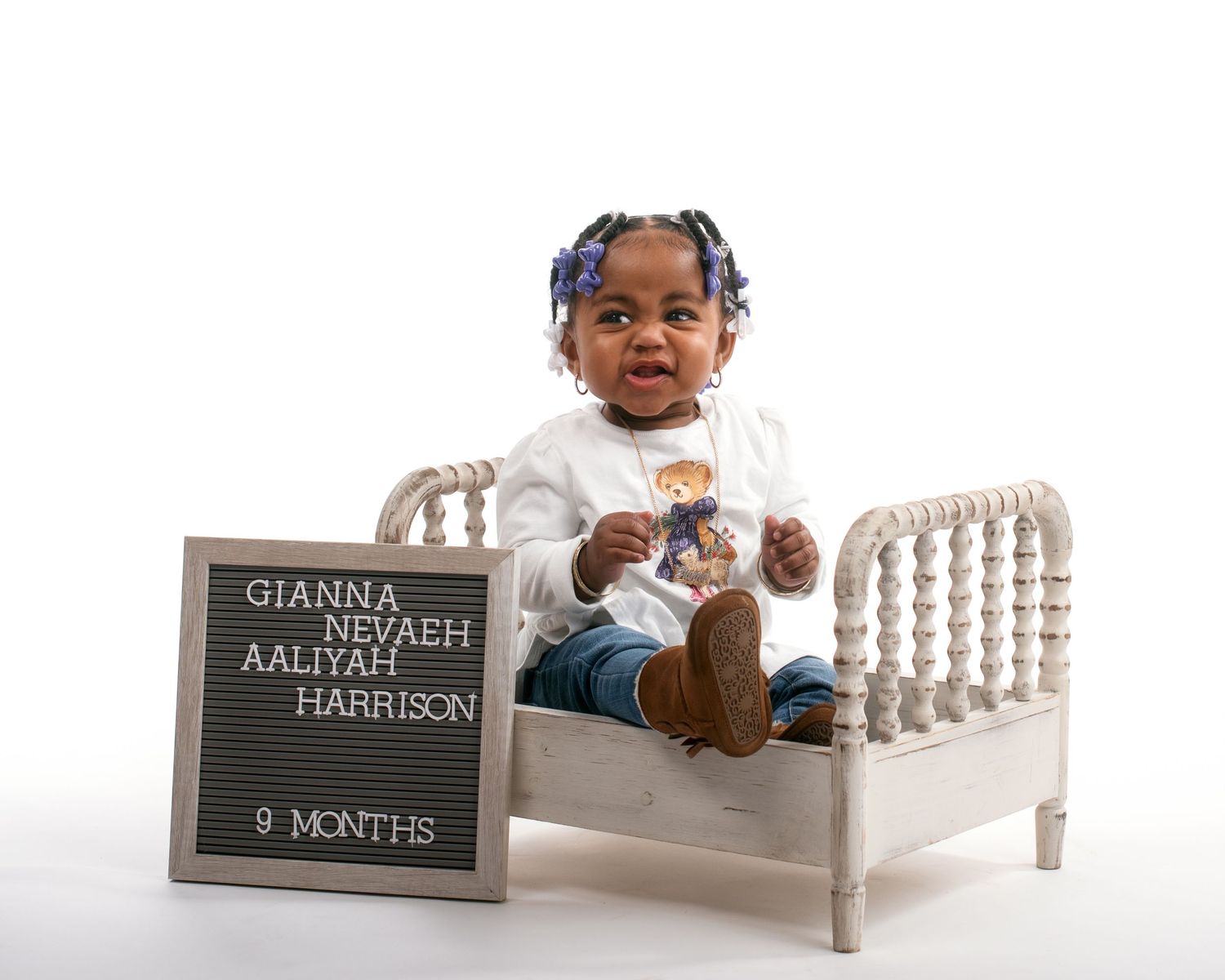 Baby girl celebrates 9 months in a white outfit on a mini bed.