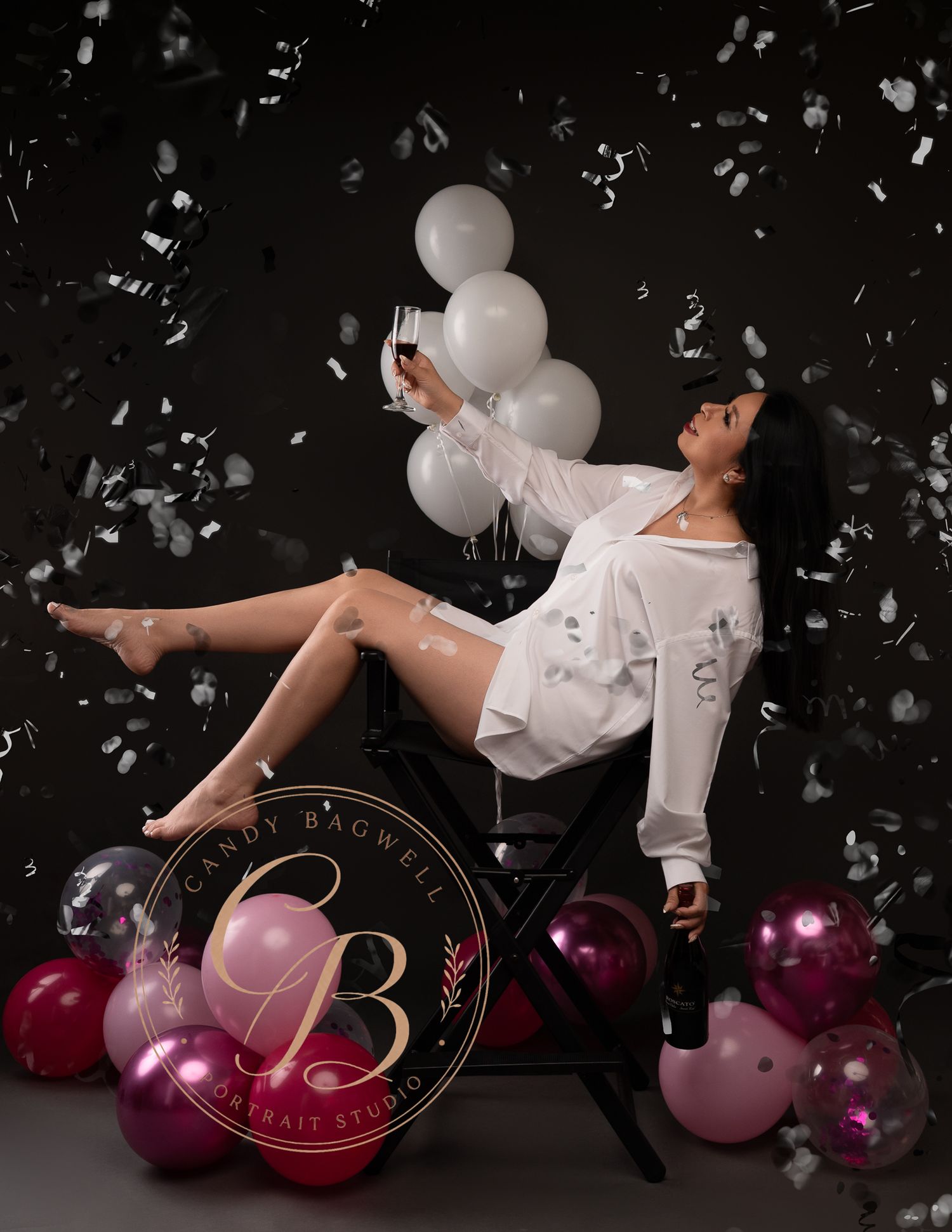 Woman in white shirt celebrates with balloons and confetti in dark studio.