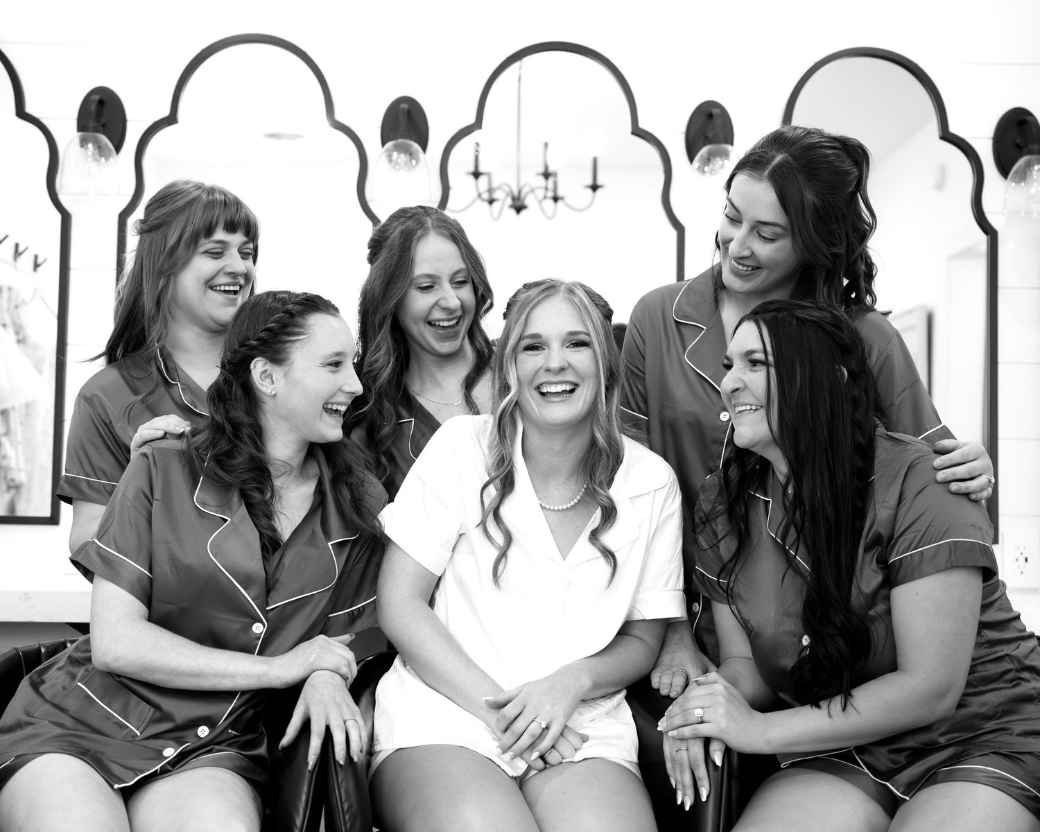 Black and white photo of bride laughing with bridesmaids in matching robes during wedding preparations.