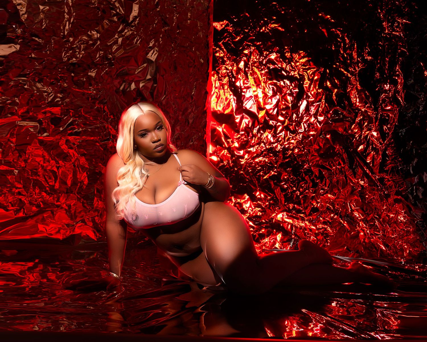 woman with blonde hair poses against dramatic red metallic foil backdrop in pink crop top and shorts.
