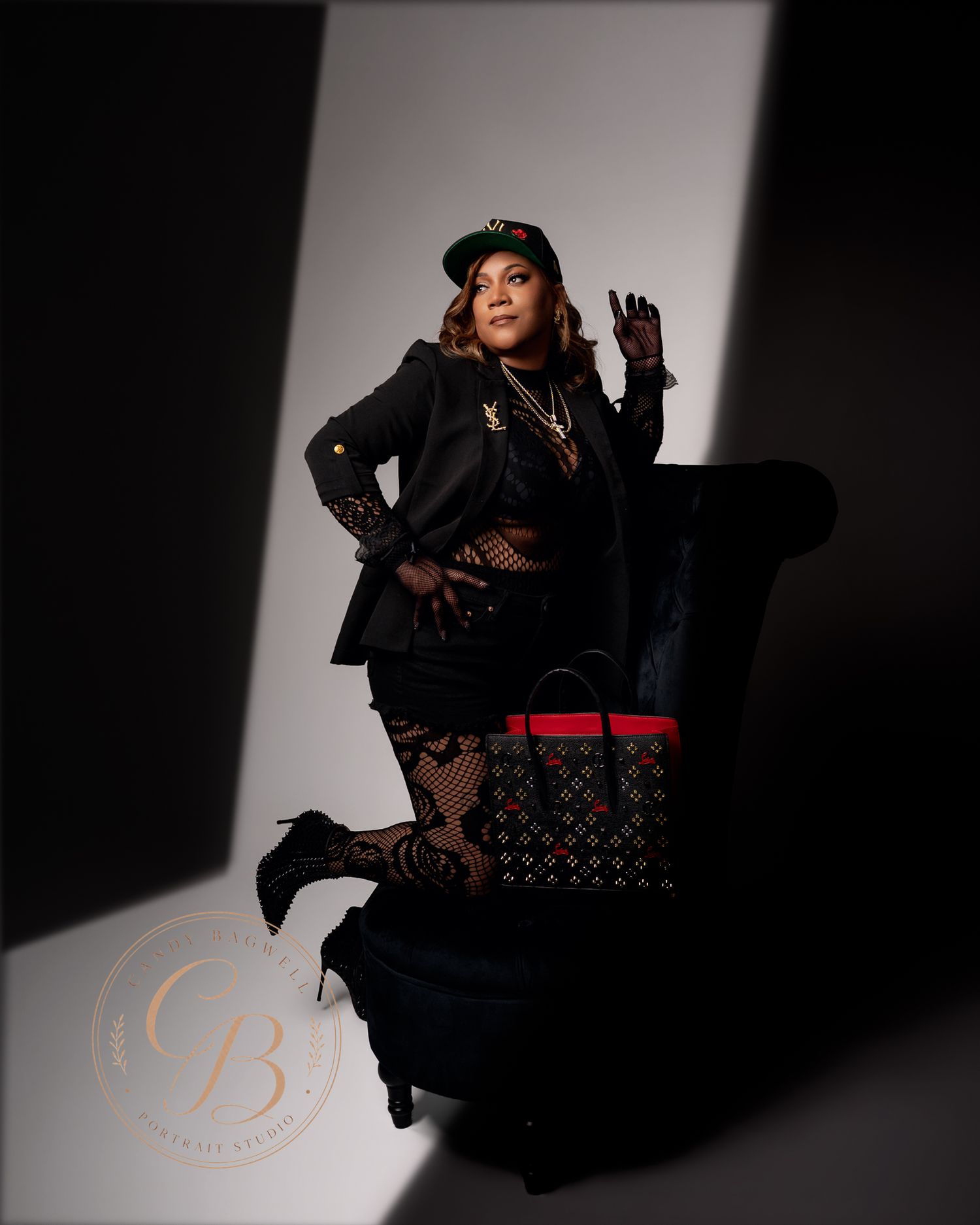 Stylish woman in all-black outfit with cap and Louis Vuitton bag posing dramatically in studio lighting.