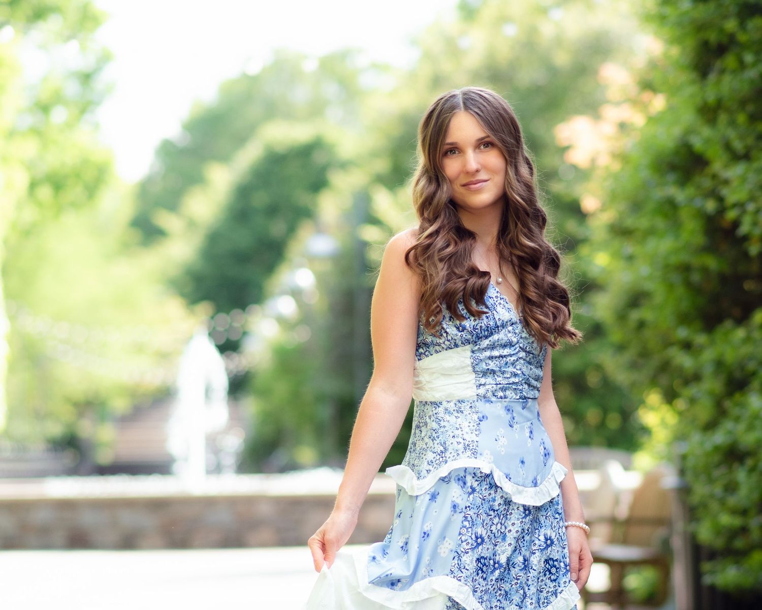 Young woman in blue floral strapless dress posing outdoors near a fountain.