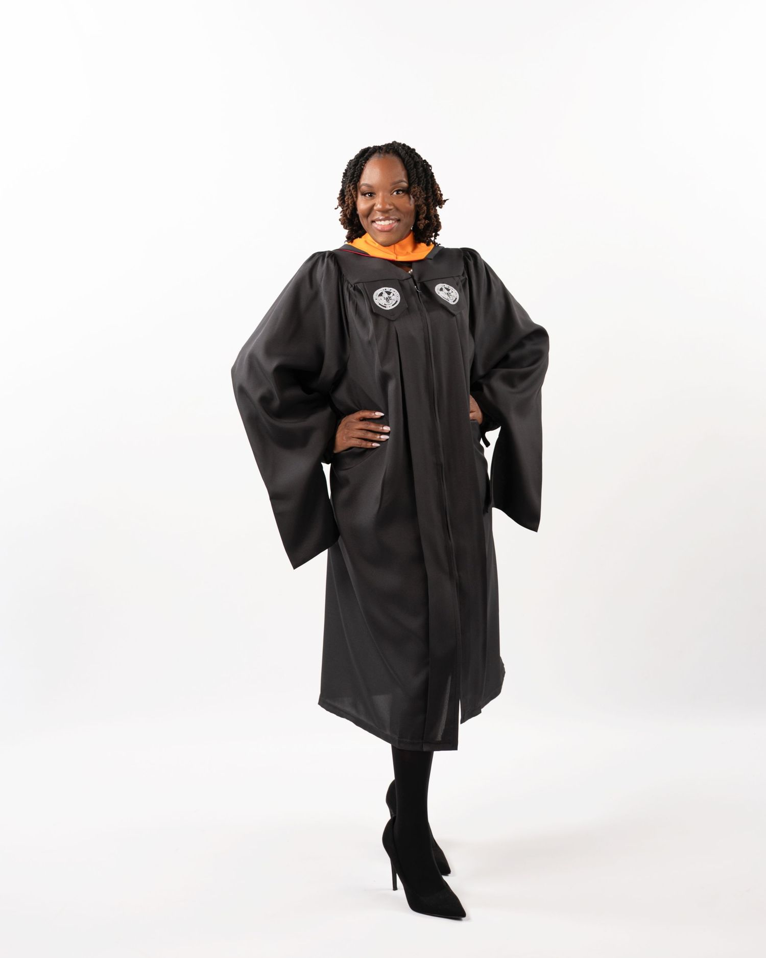 Graduate smiling in black doctoral gown with orange hood and medallions.