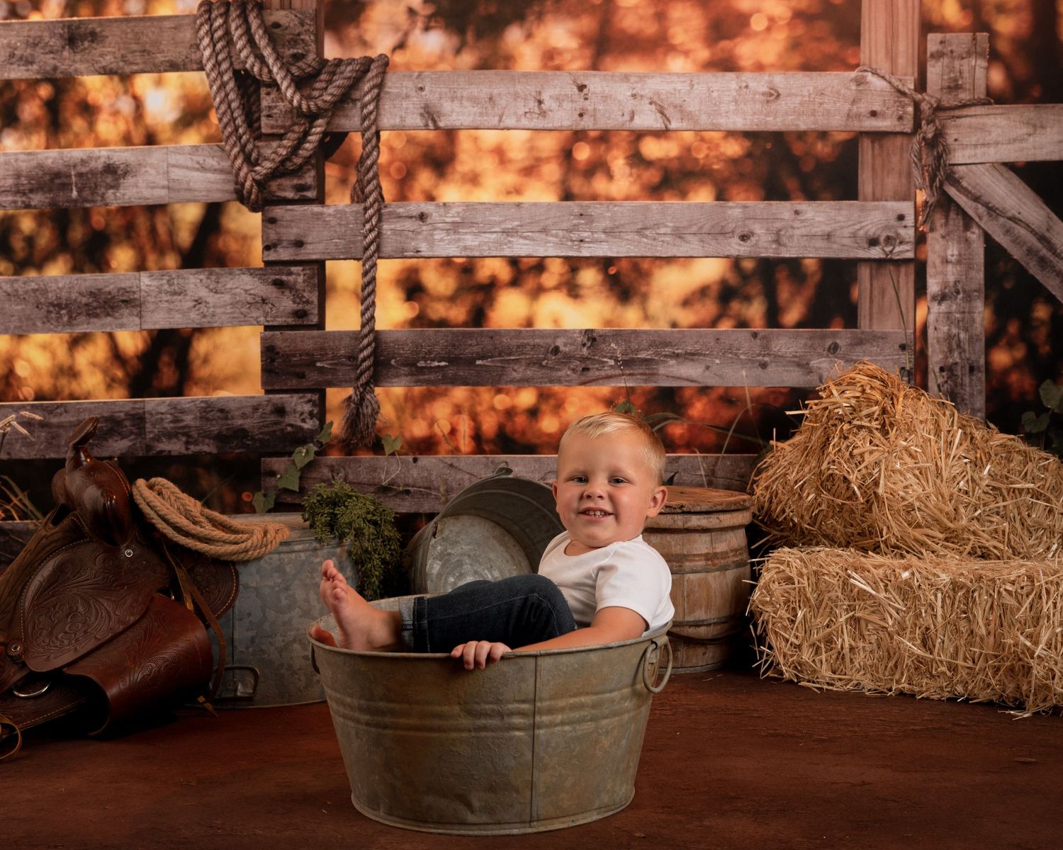 Happy baby sitting in a metal tub with rustic farm-themed backdrop and hay bales.