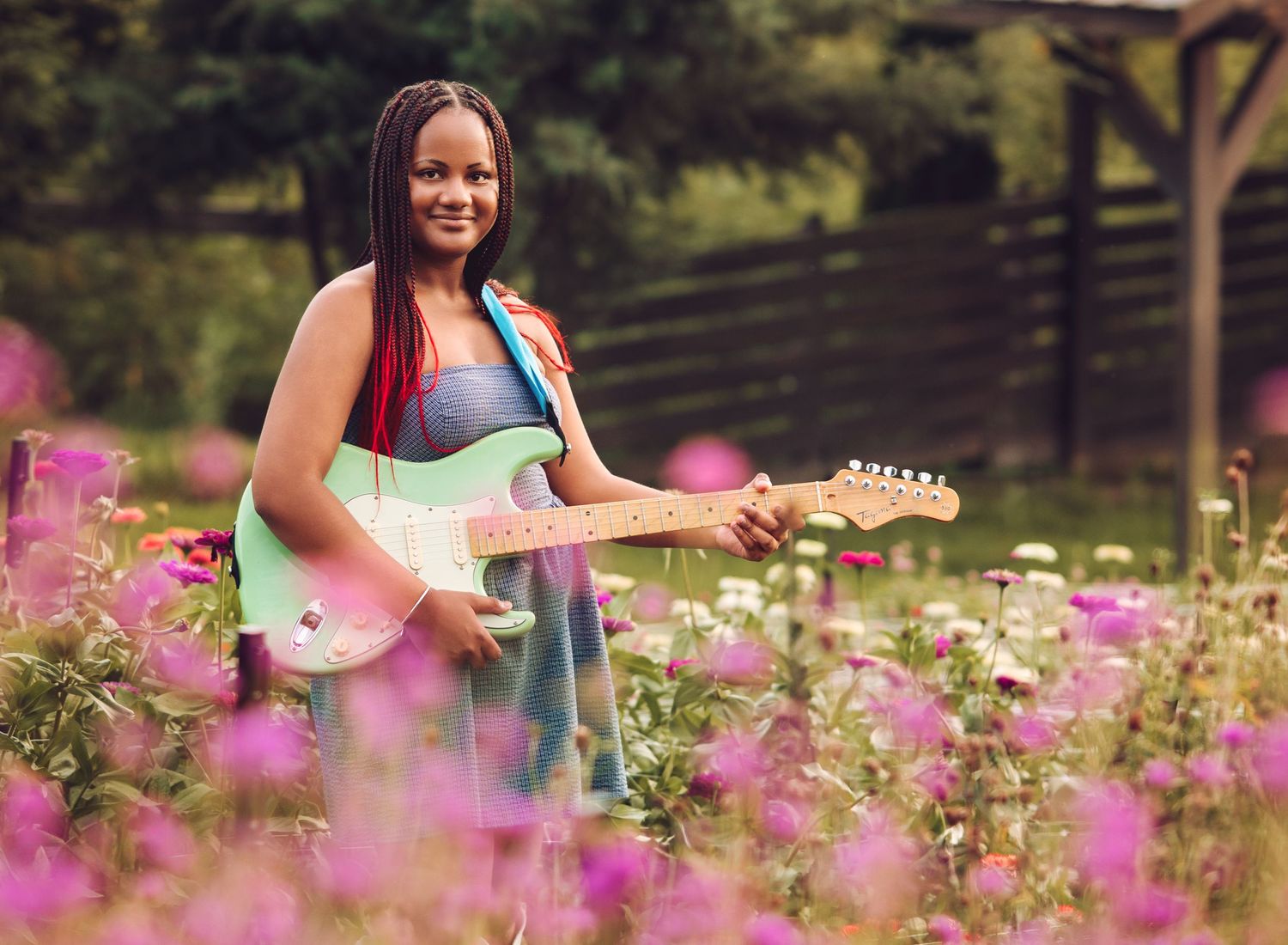 Young woman holding a mint green guitar while standing in a vibrant pink flower garden.