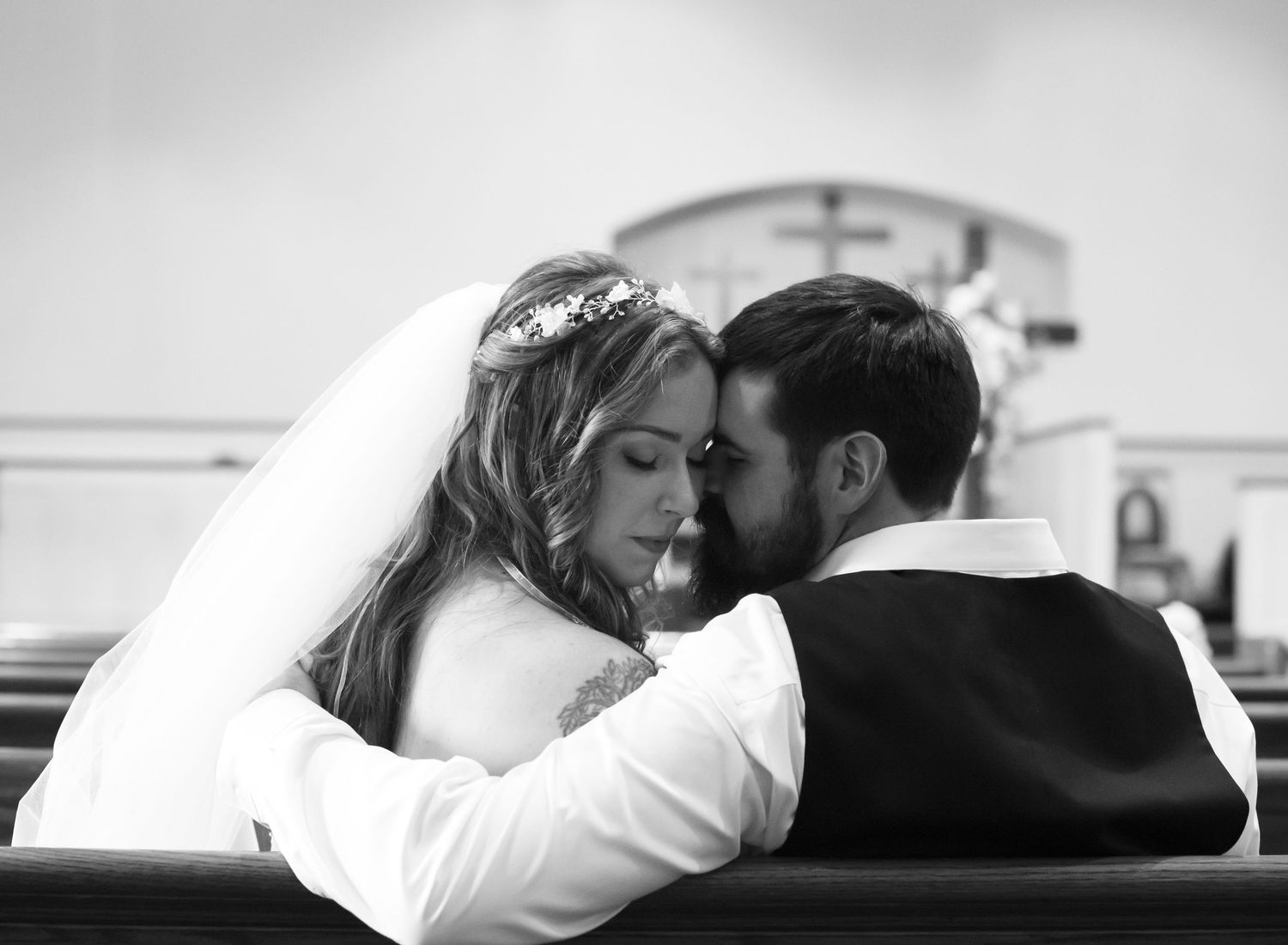 Black and white photo of bride and groom sharing an intimate moment in a church pew on their wedding day.