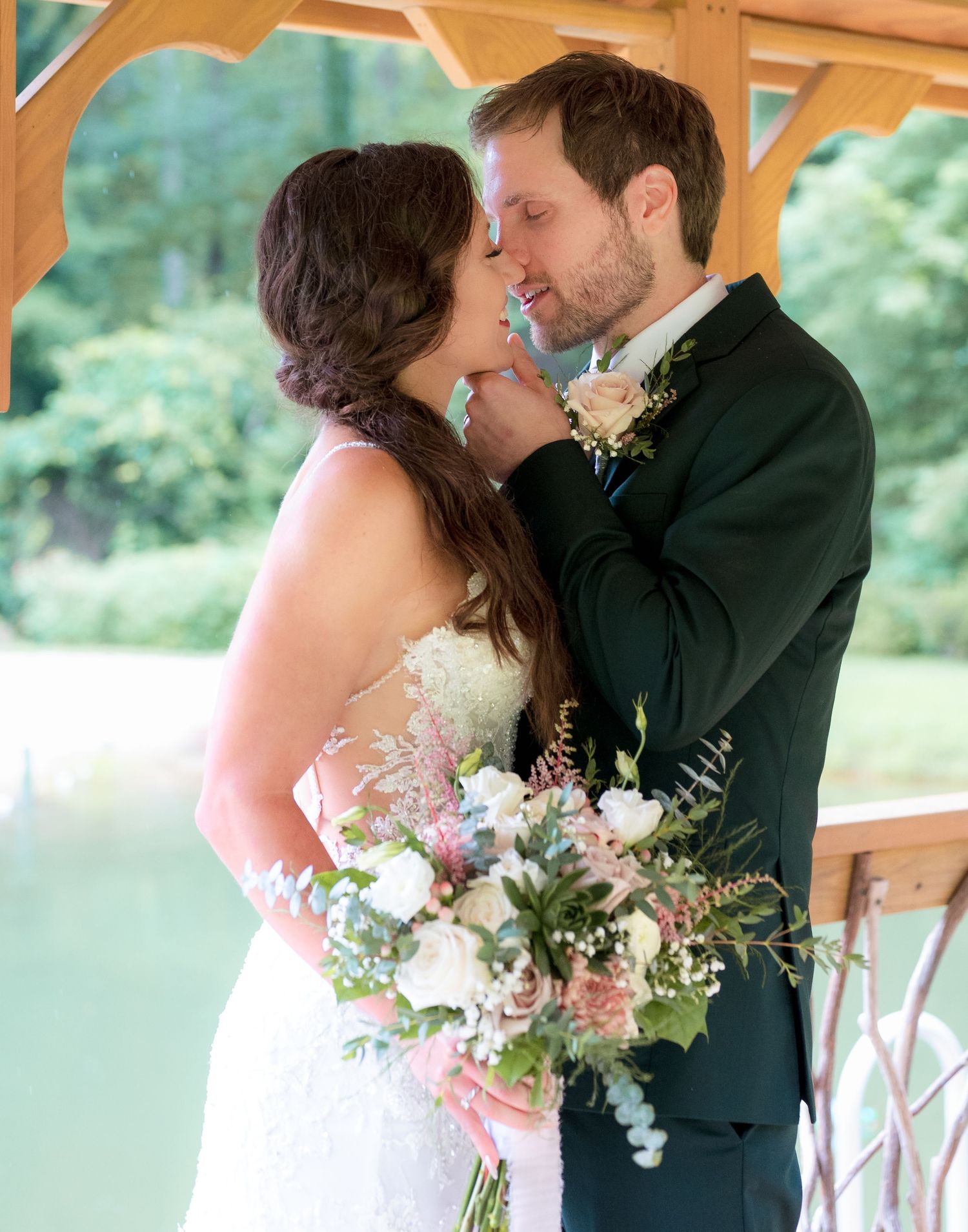 Bride and groom share intimate moment under pavilion with lush greenery background.