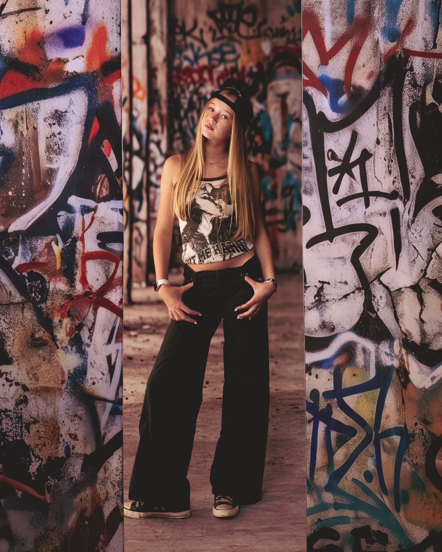 A teenage girl in wide-leg pants poses confidently in front of colorful graffiti-covered walls outdoors.