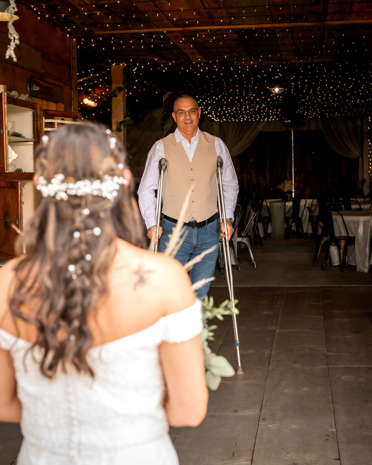 Emotional father walking with crutches toward bride in rustic barn wedding reception.