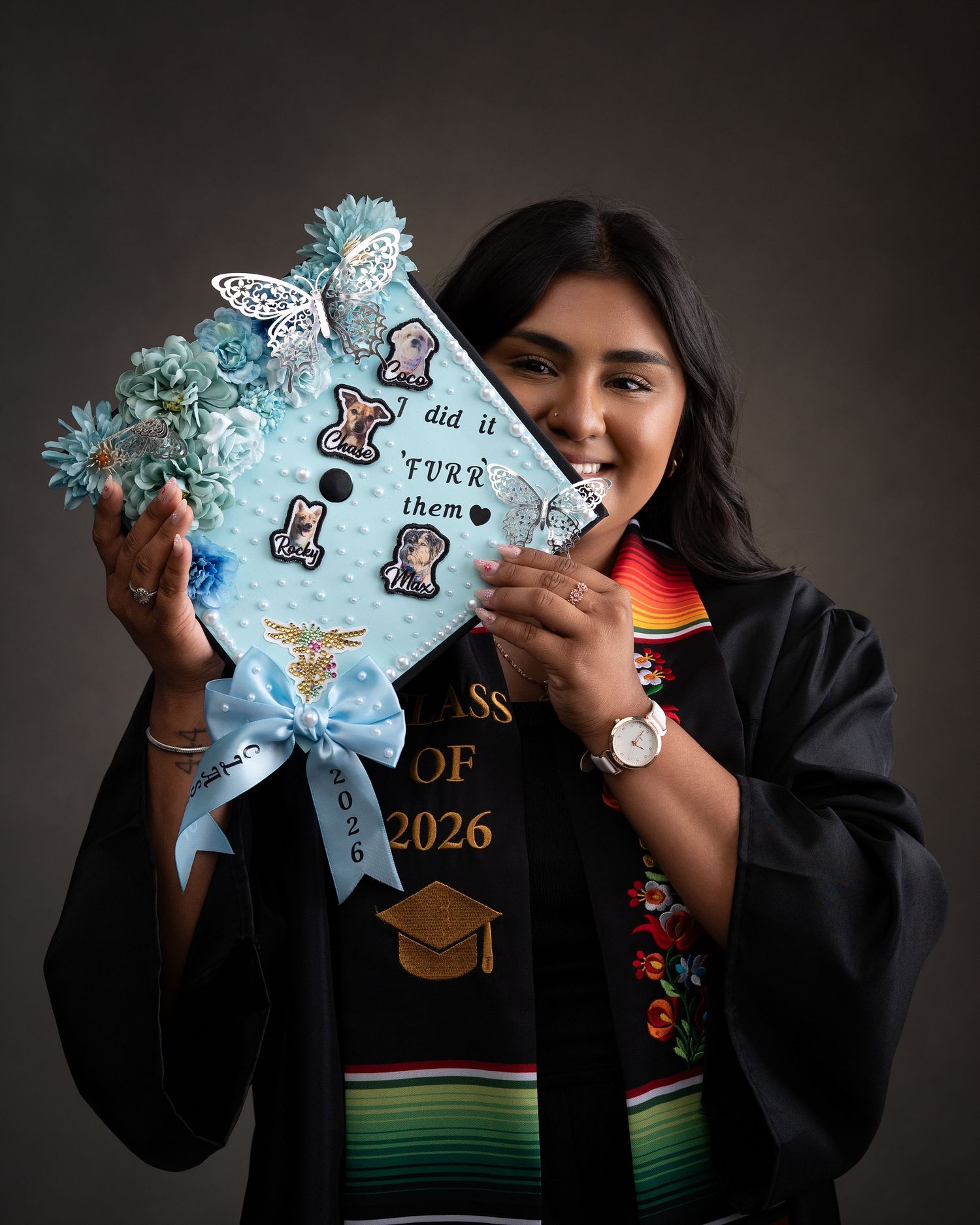 Graduate holds decorated cat-themed mortarboard cap with 'did it FURR them' text, wearing black gown and colorful sash.
