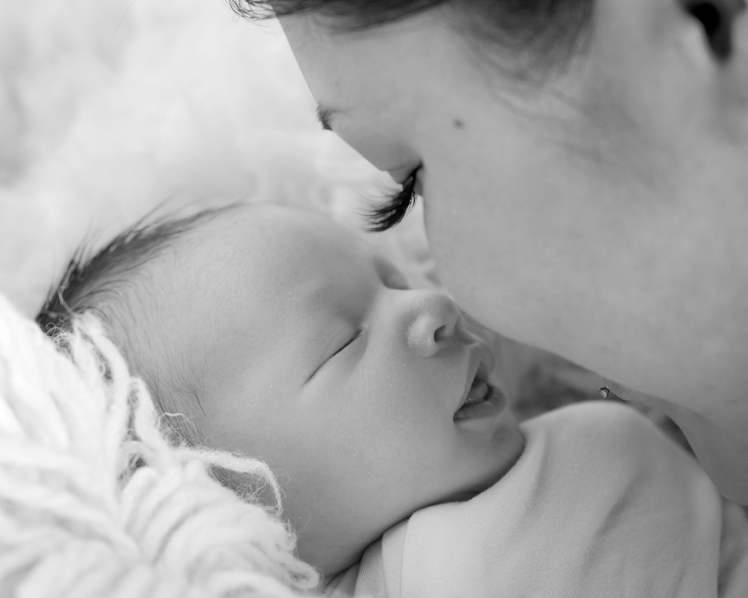 Black and white close-up of mother gently touching foreheads with her sleeping newborn baby.