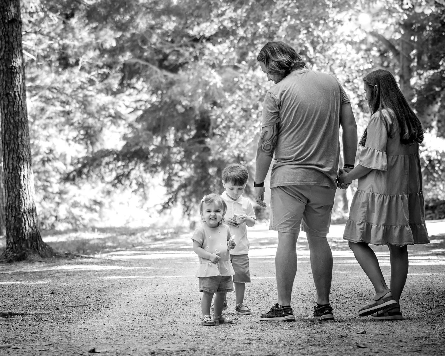 Black and white photo of a father walking with three young children along a shaded park path.
