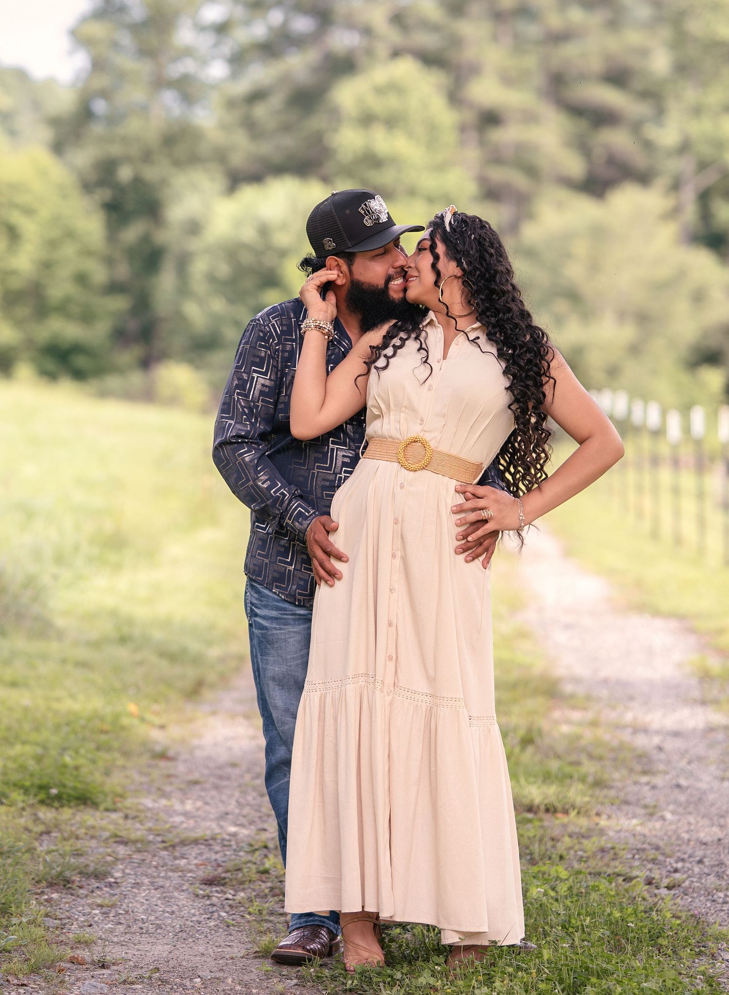 Couple sharing a kiss on a scenic outdoor path during maternity shoot.