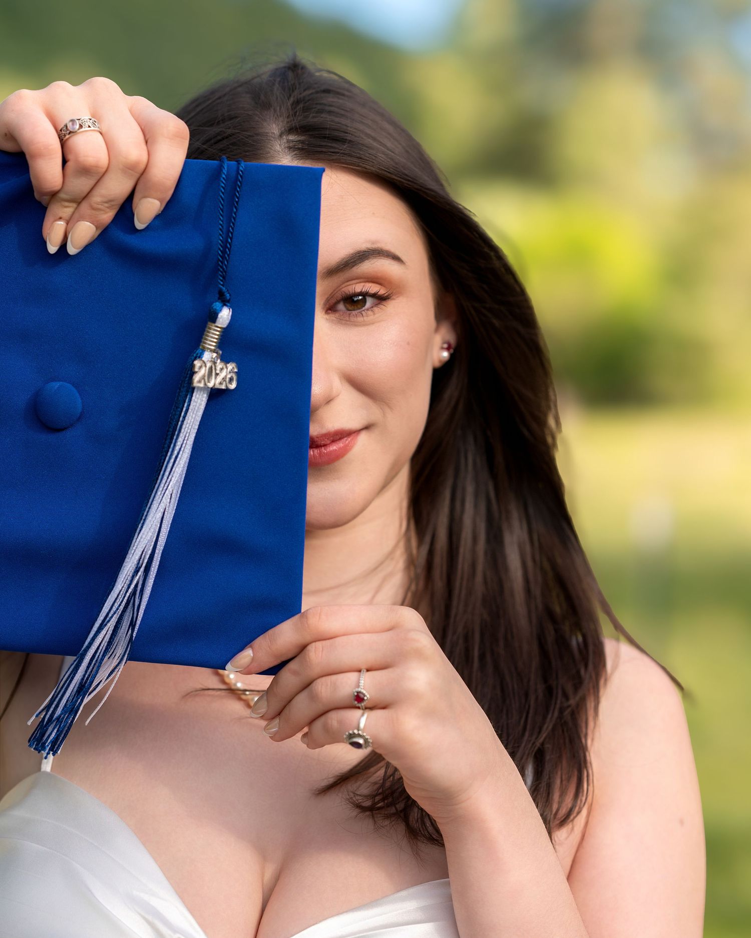 Graduate holds blue cap covering half her face revealing elegant makeup and dark hair.
