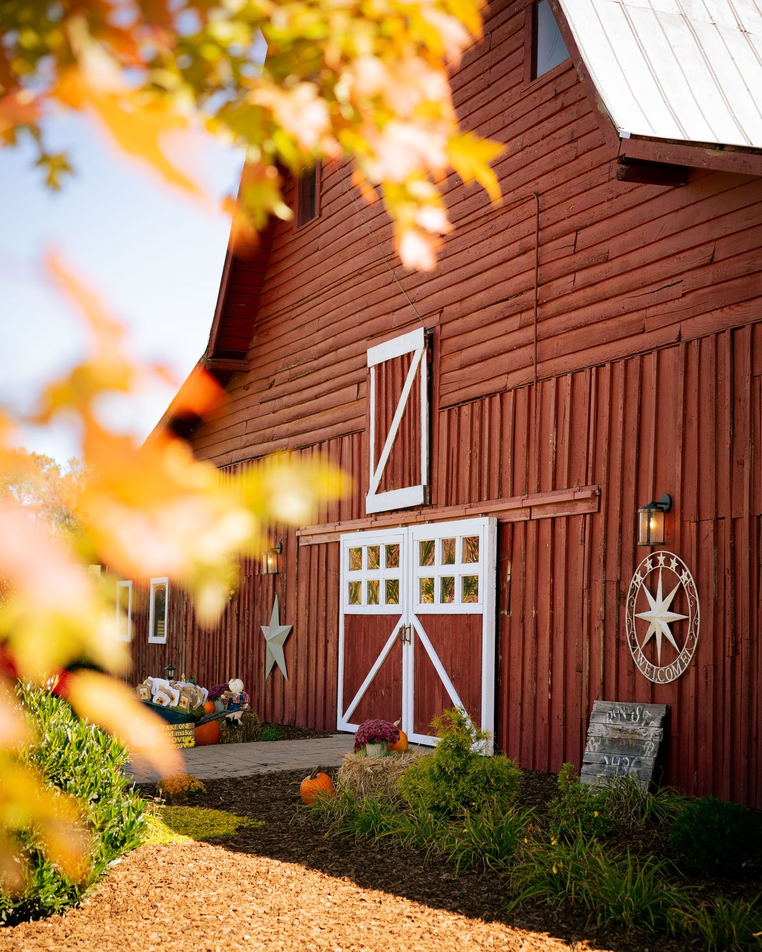 Classic red barn wedding venue decorated with pumpkins and autumn foliage under a bright blue sky.