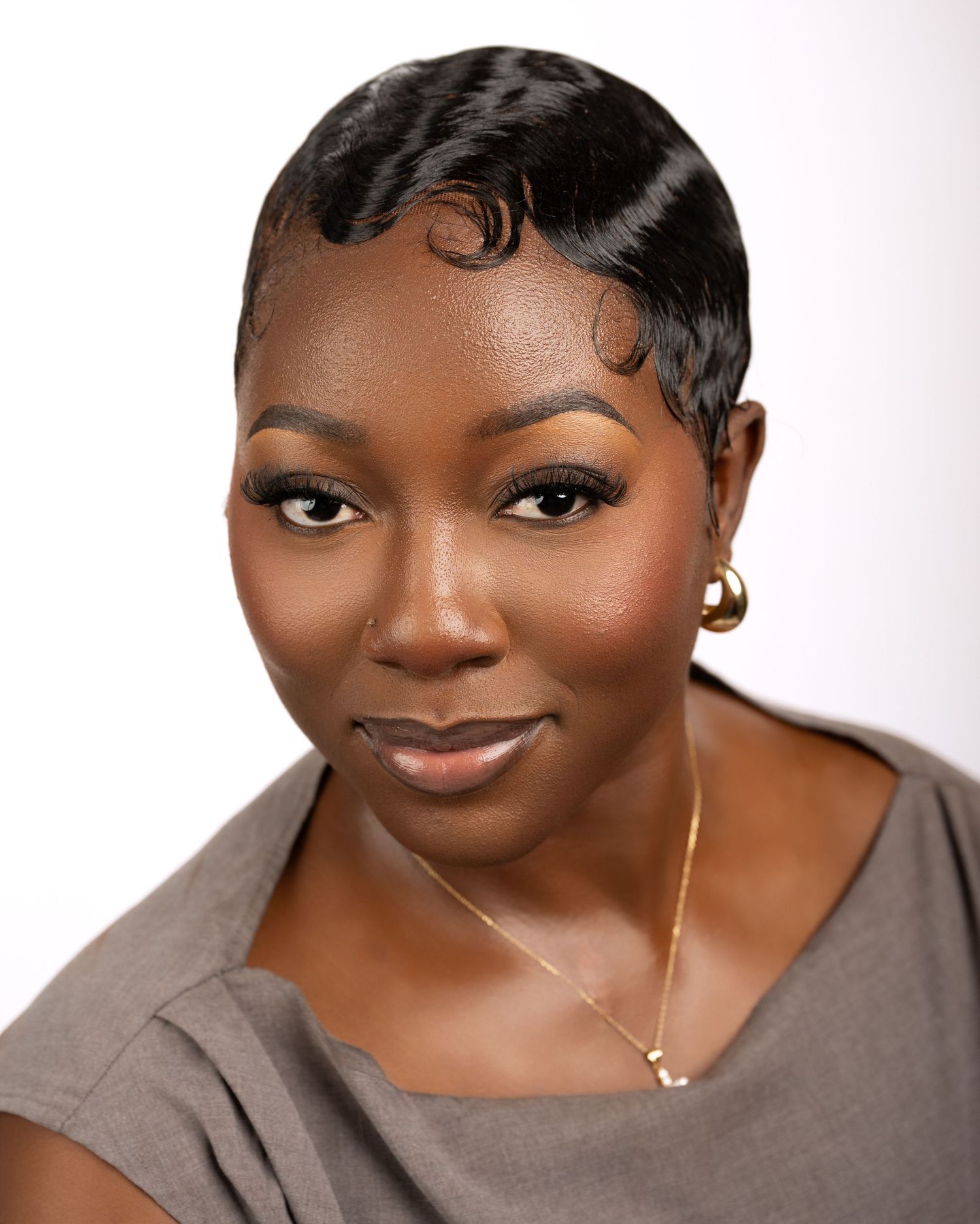 Professional headshot of a woman wearing a gray top and gold jewelry against a white background.