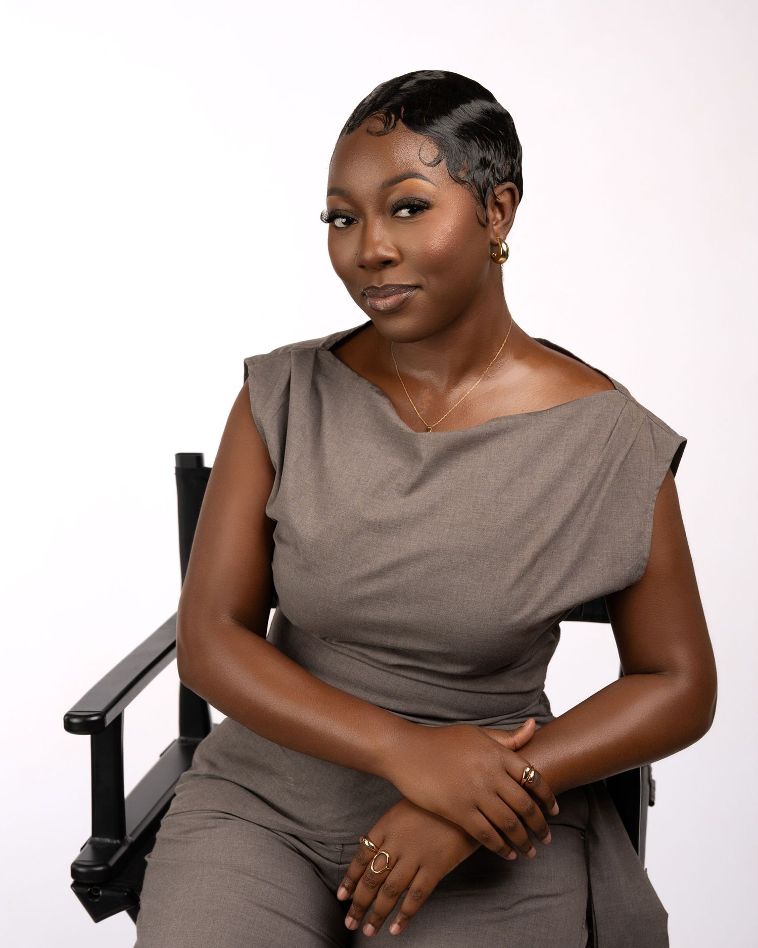 Professional woman in gray dress seated confidently in director's chair against white background.