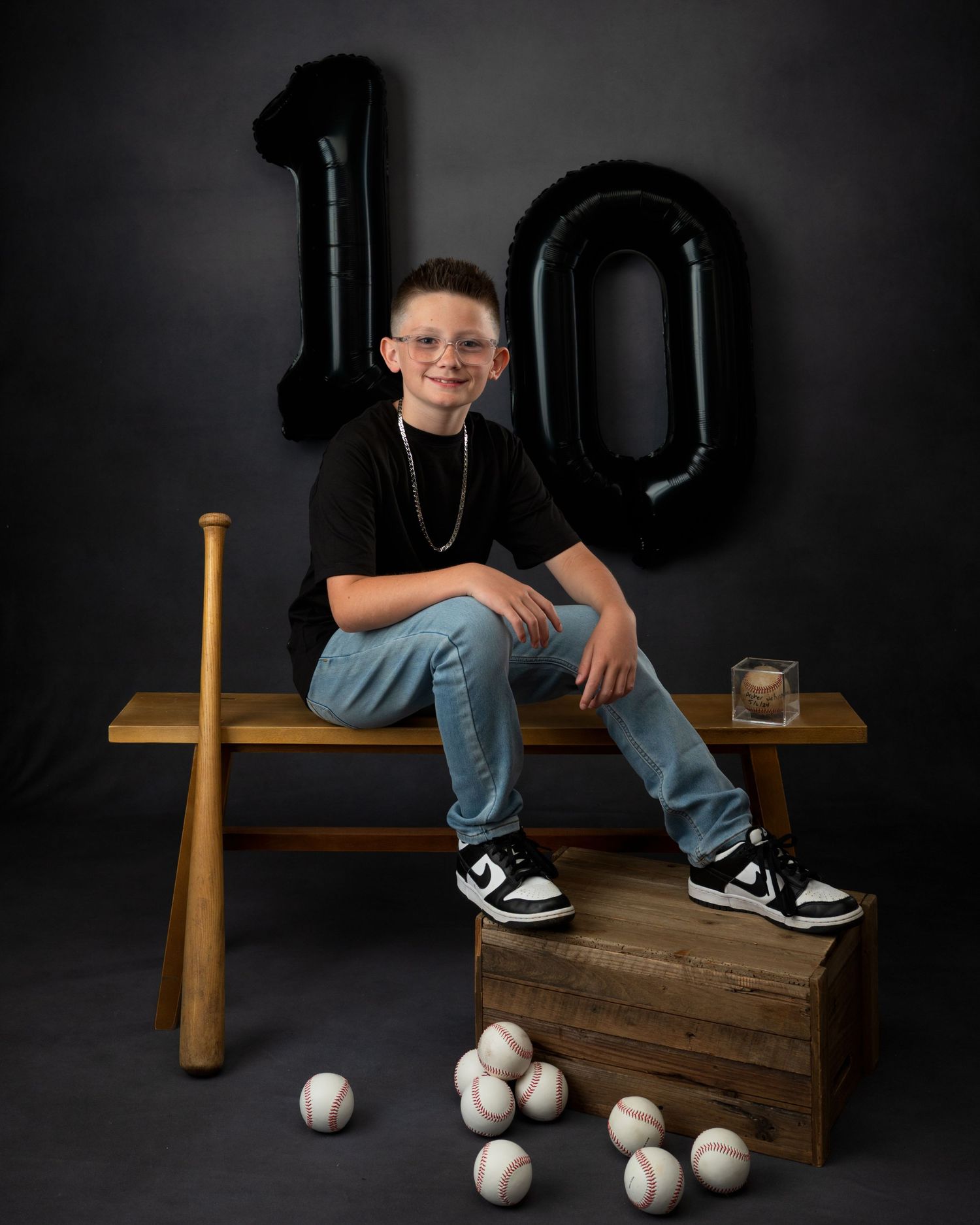 Boy celebrates 10th birthday with baseball-themed portrait featuring bat, balls, and black balloons.