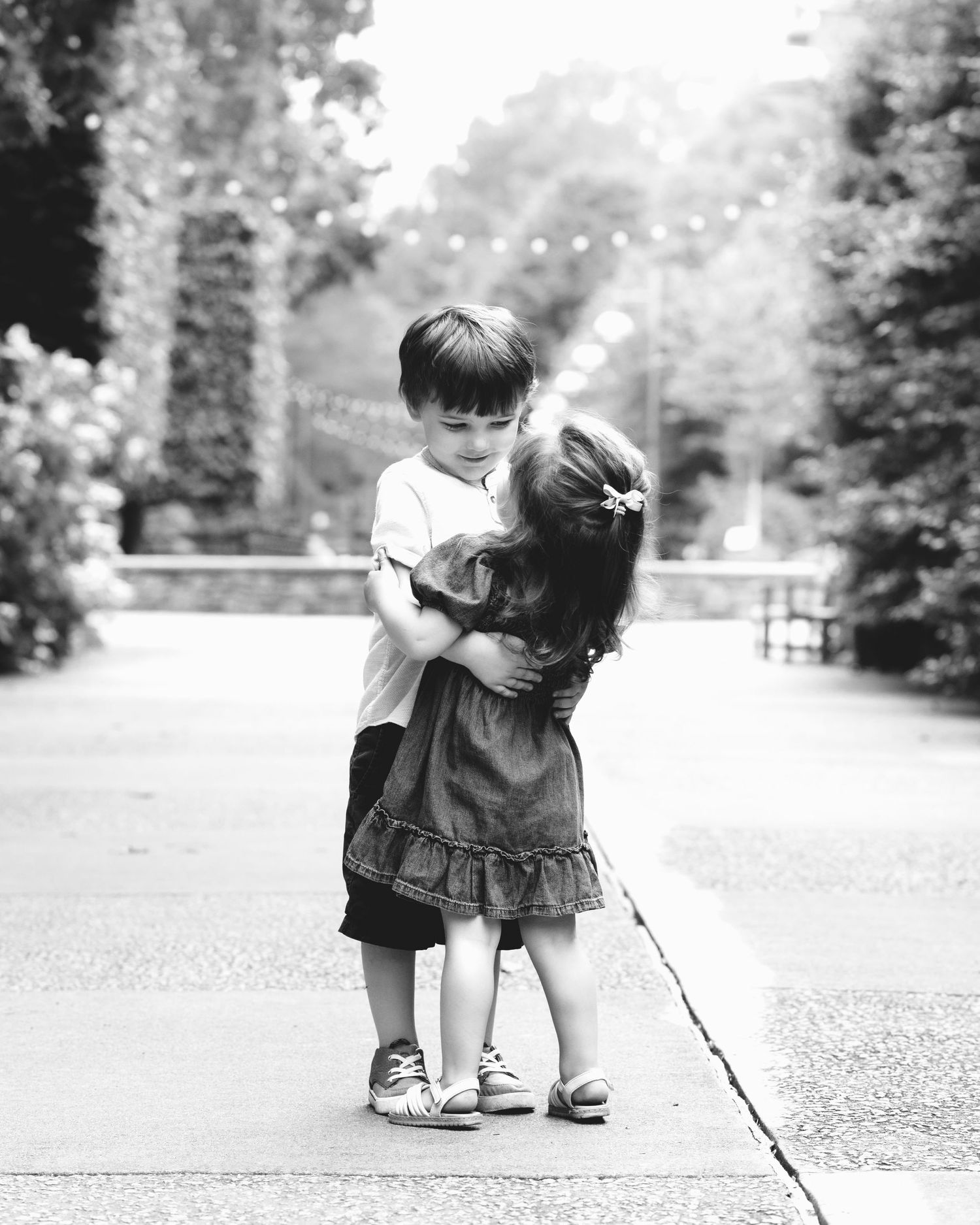 Two young children sharing a sweet hug on a garden path in black and white photo.