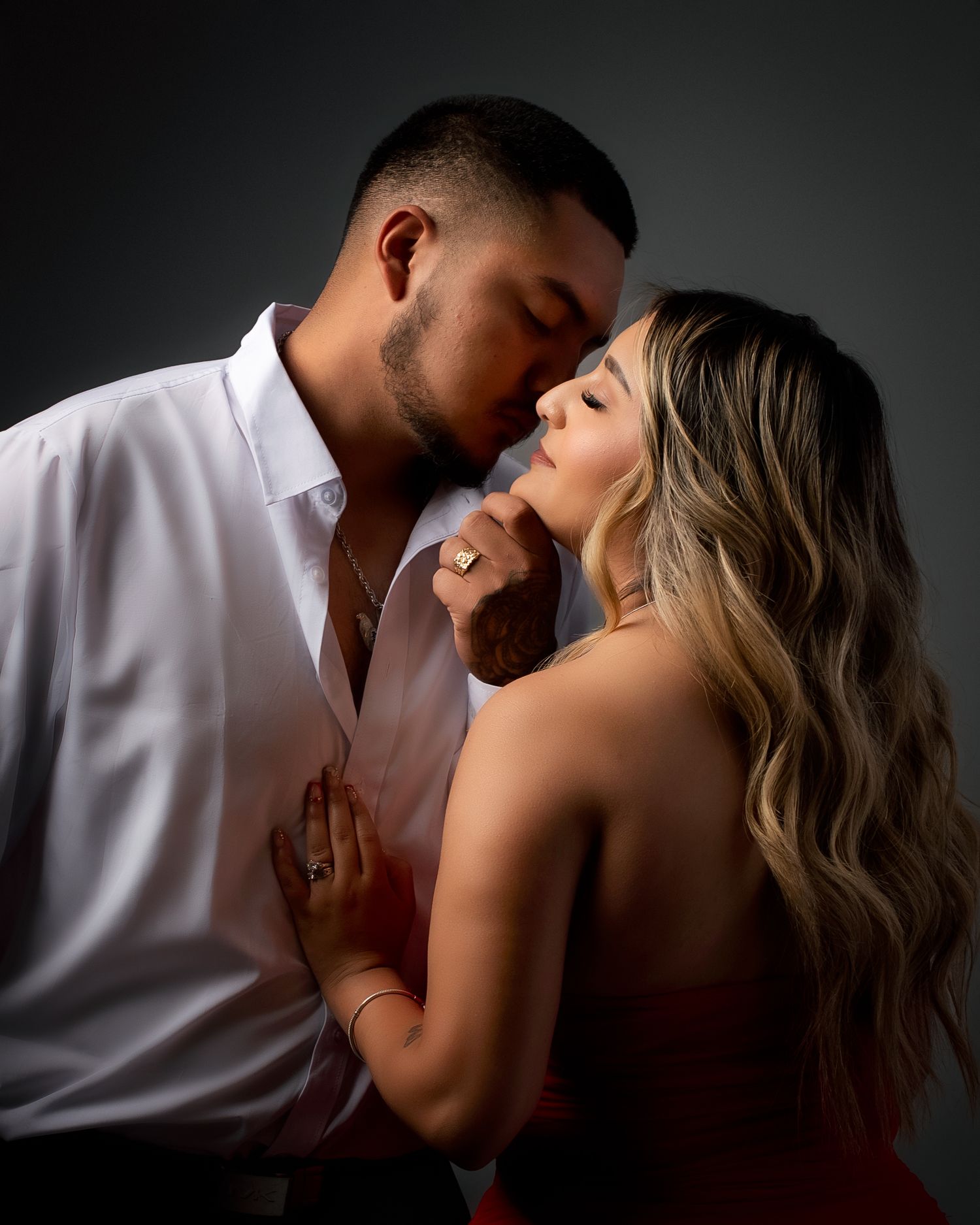 Intimate couple portrait with woman in red dress and man in white shirt in dark studio.
