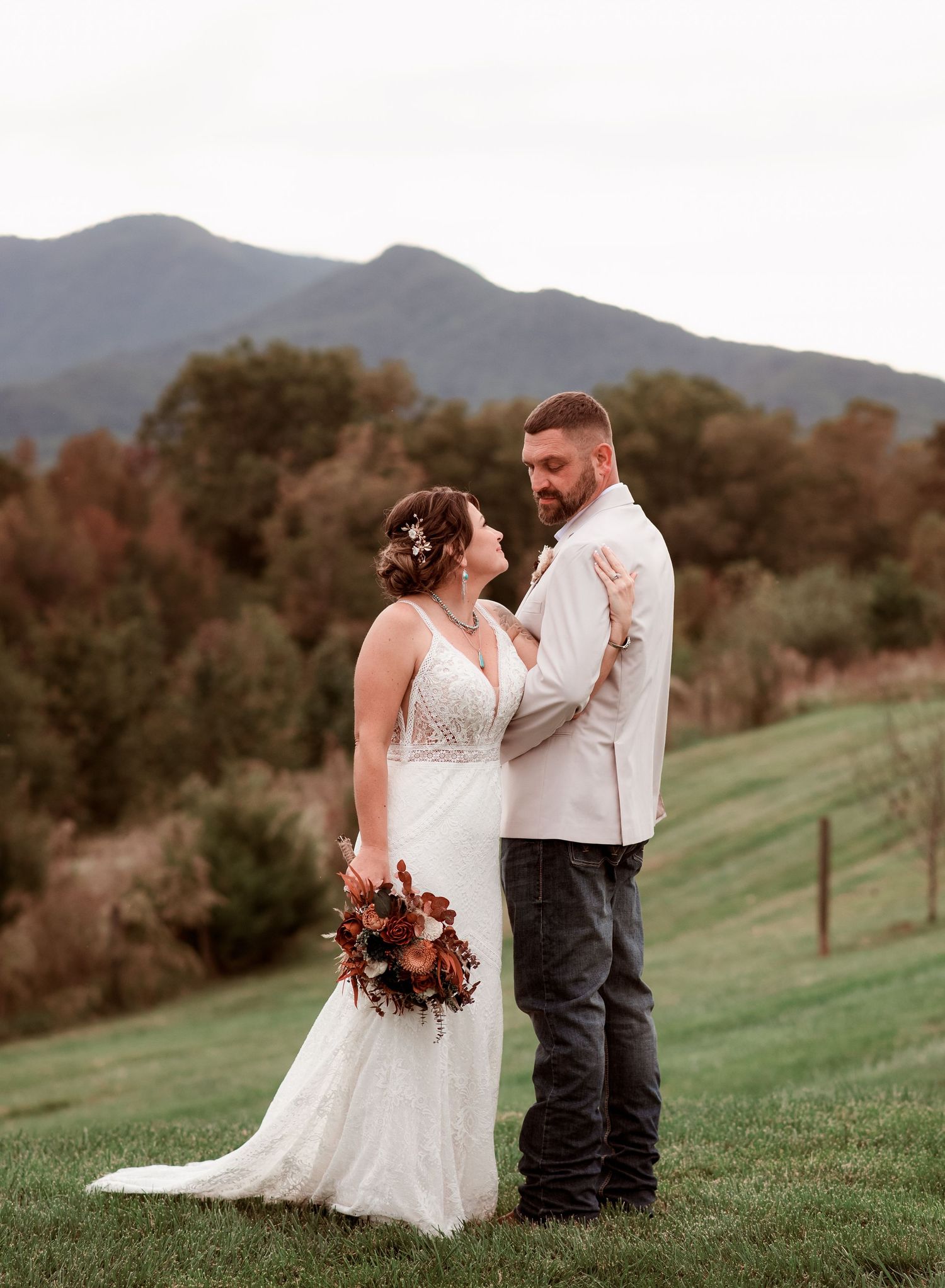 Bride and groom pose together with colorful autumn mountain scenery at outdoor wedding.
