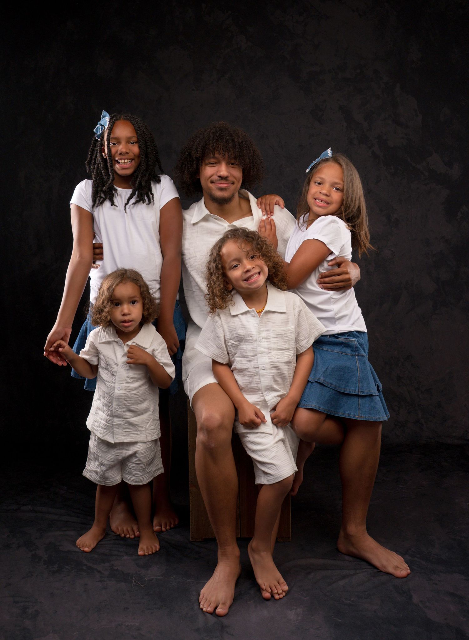 Father posing with four children in coordinated white and denim outfits in studio portrait.